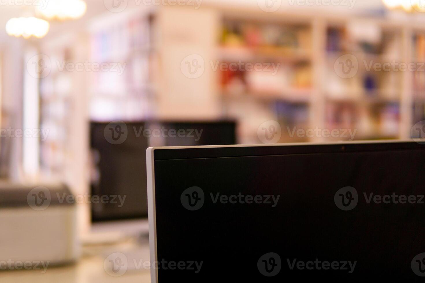 Blurred interior of traditional library with computer monitor on a foreground and bookshelfs photo