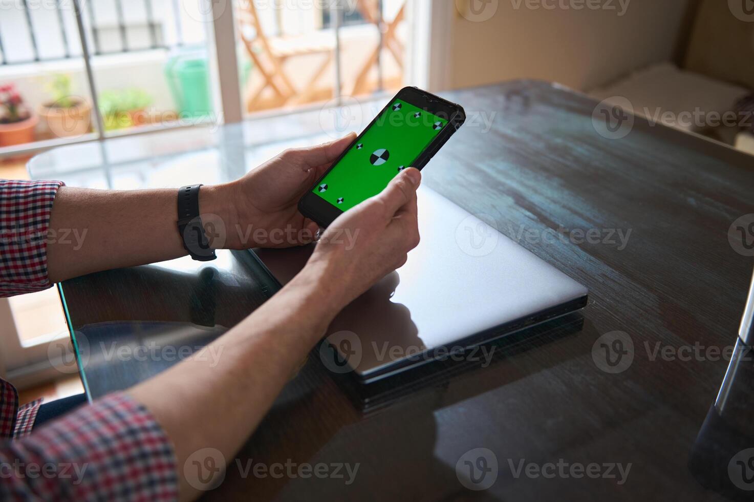 Man Using Smartphone With Green Screen While Seated by a Laptop photo