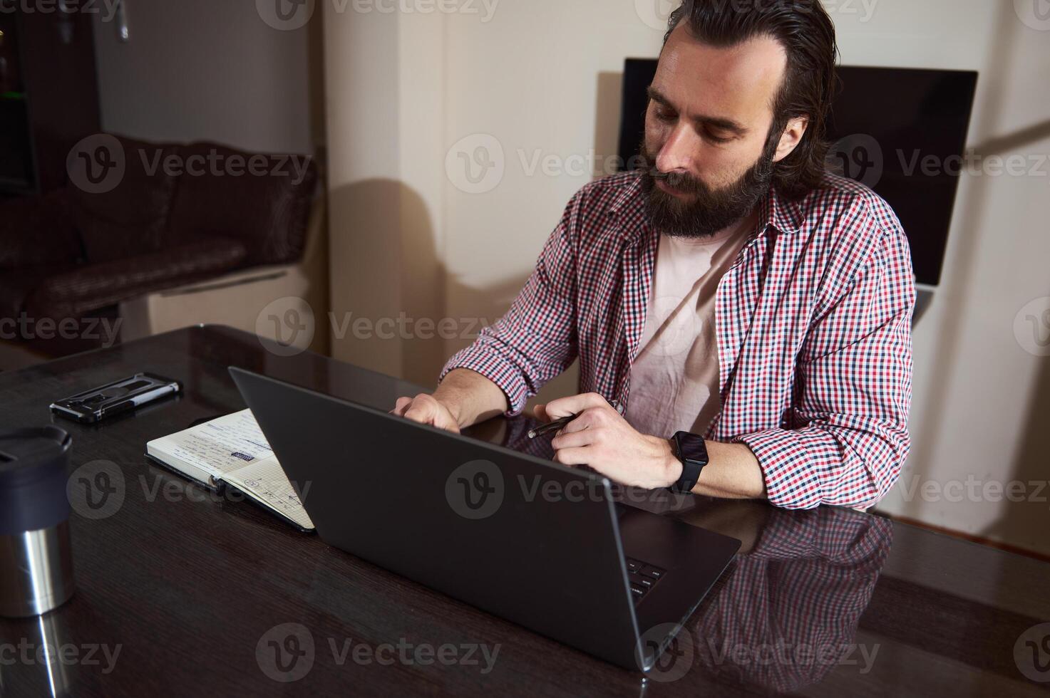 Focused Man Working on Laptop While Taking Notes in a Home Office photo