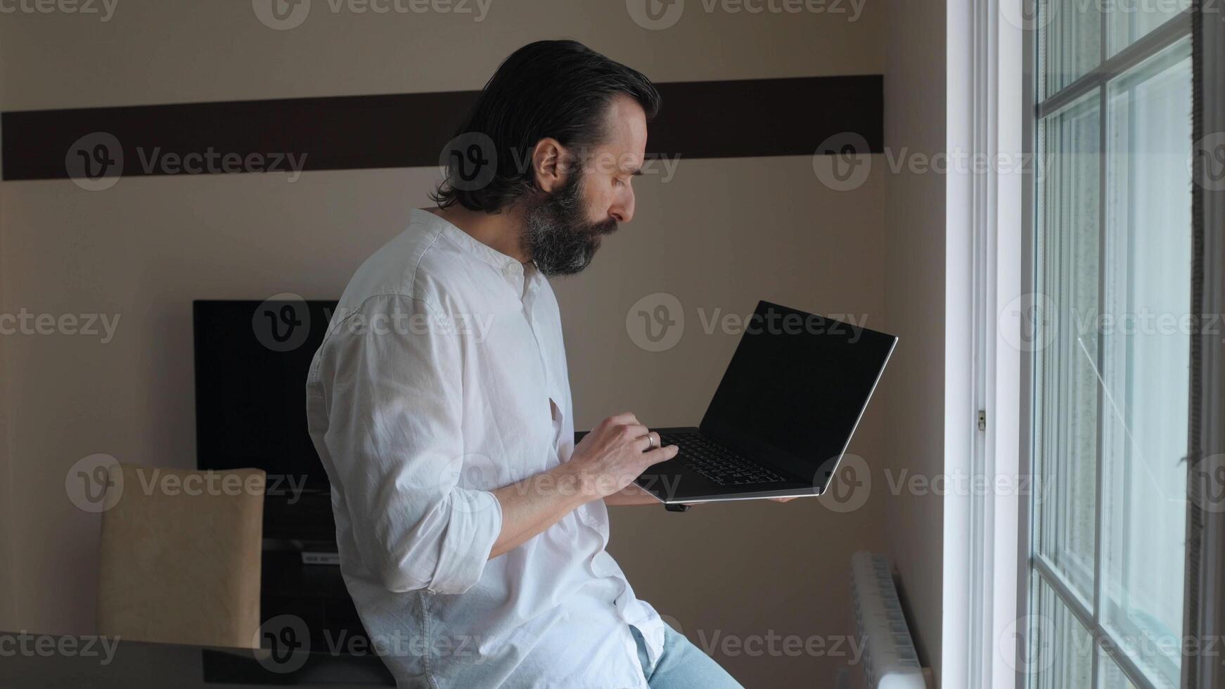 Focused Bearded Male Using Laptop by Window in Bright Modern Office photo