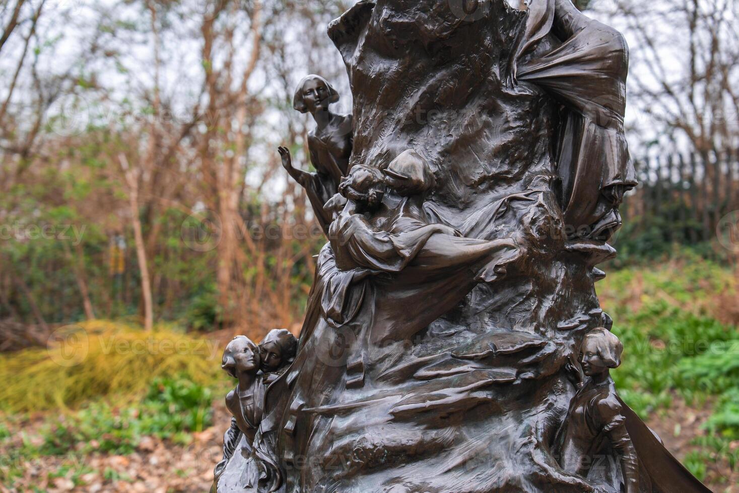 Outdoor bronze sculpture featuring children and adults carved into a tree like structure, set in a natural park environment with trees and shrubs. photo