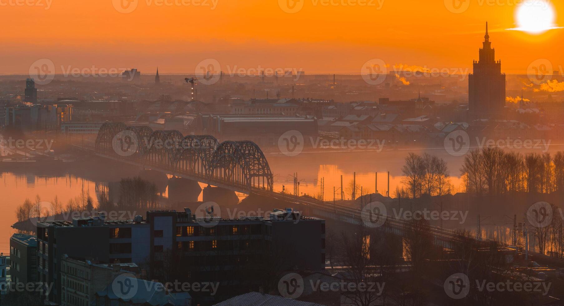 A warm sunrise illuminates Riga, Latvia, with the arched railway bridge over the Daugava River and the Latvian Academy of Sciences in the background. photo