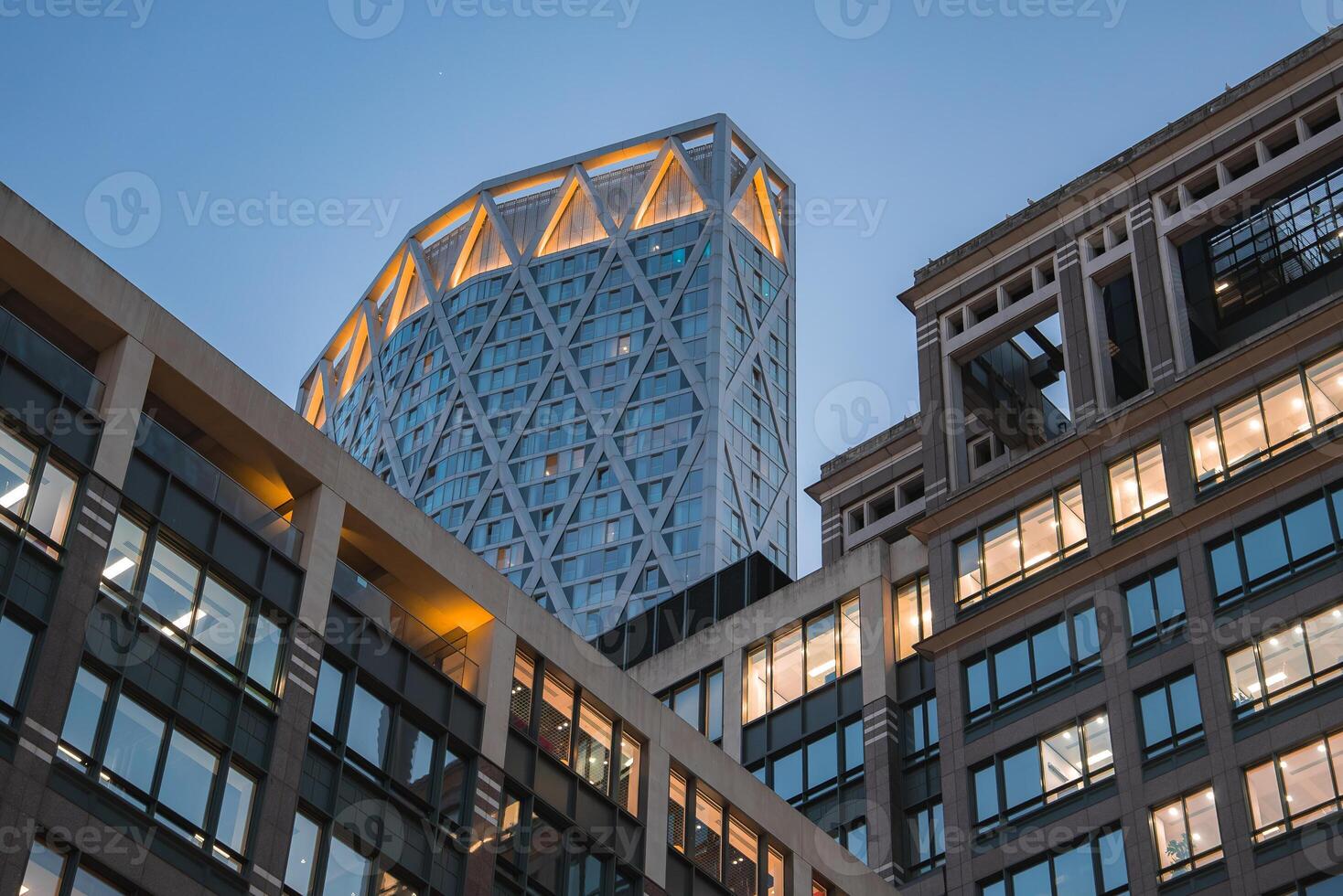Evening view of 22 Bishopsgate in London with its illuminated diamond patterned facade, surrounded by lit office buildings under a clear sky. photo
