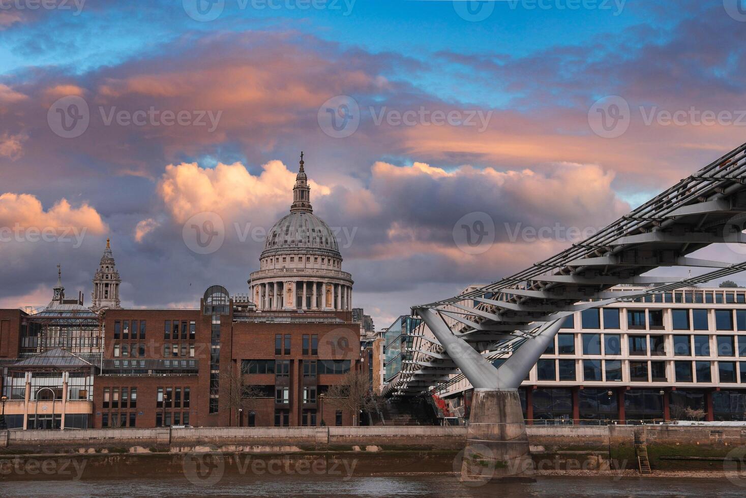 View of St. Paul's Cathedral with its dome at sunset, the Millennium Bridge crossing the River Thames, and a mix of historic and modern architecture. photo