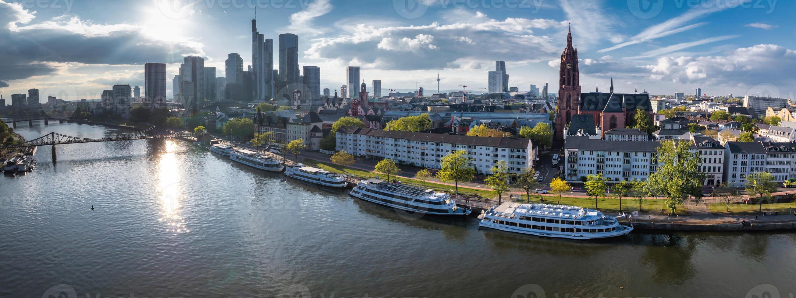 Aerial view of Frankfurt, Germany, featuring the Main River, Commerzbank Tower, Frankfurt Cathedral, Eiserner Steg bridge, and docked boats. photo