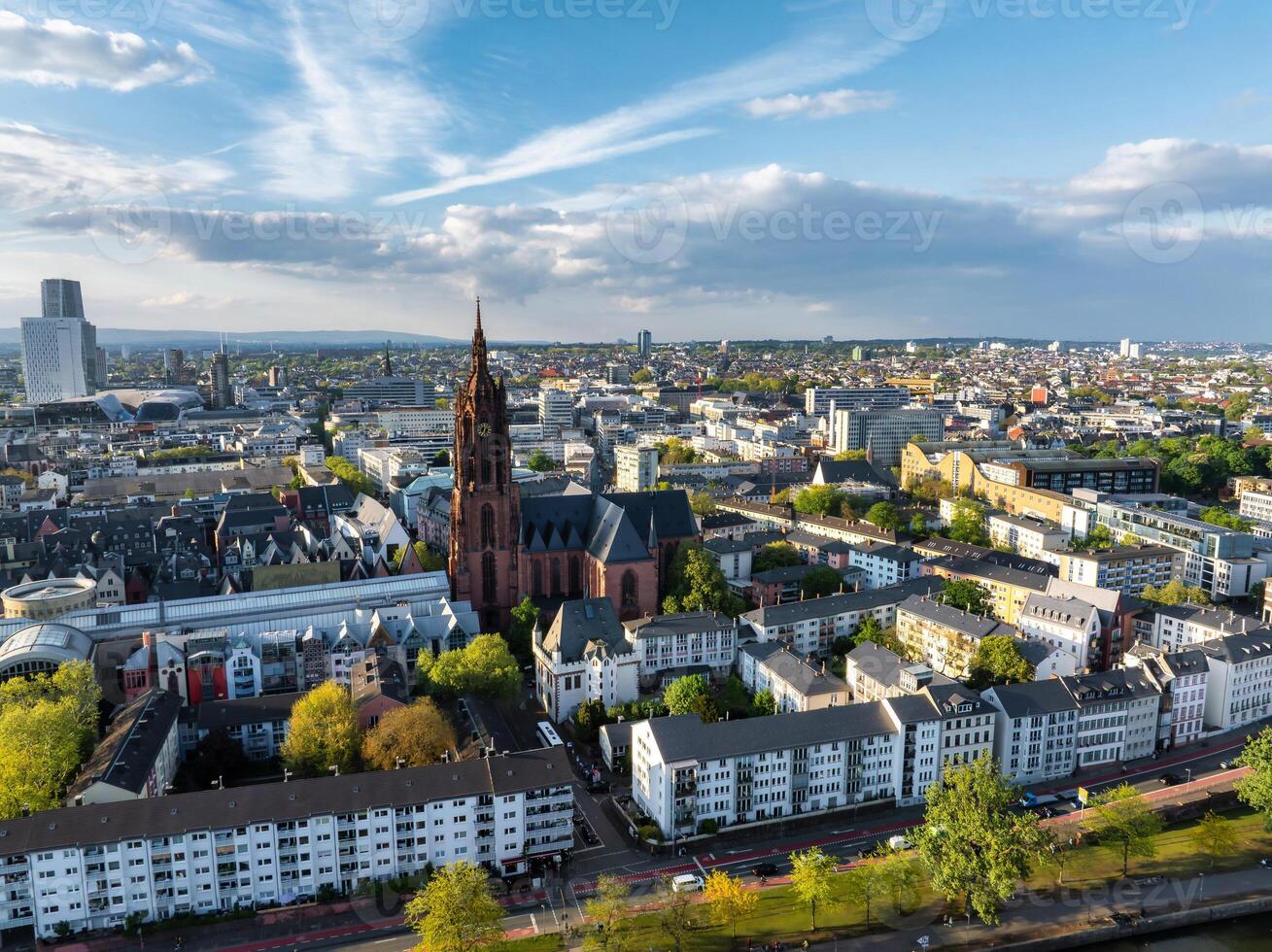 Aerial image of Frankfurt, Germany, highlighting St. Paul's Church, modern and traditional buildings, tree lined streets, and a partly cloudy sky. photo