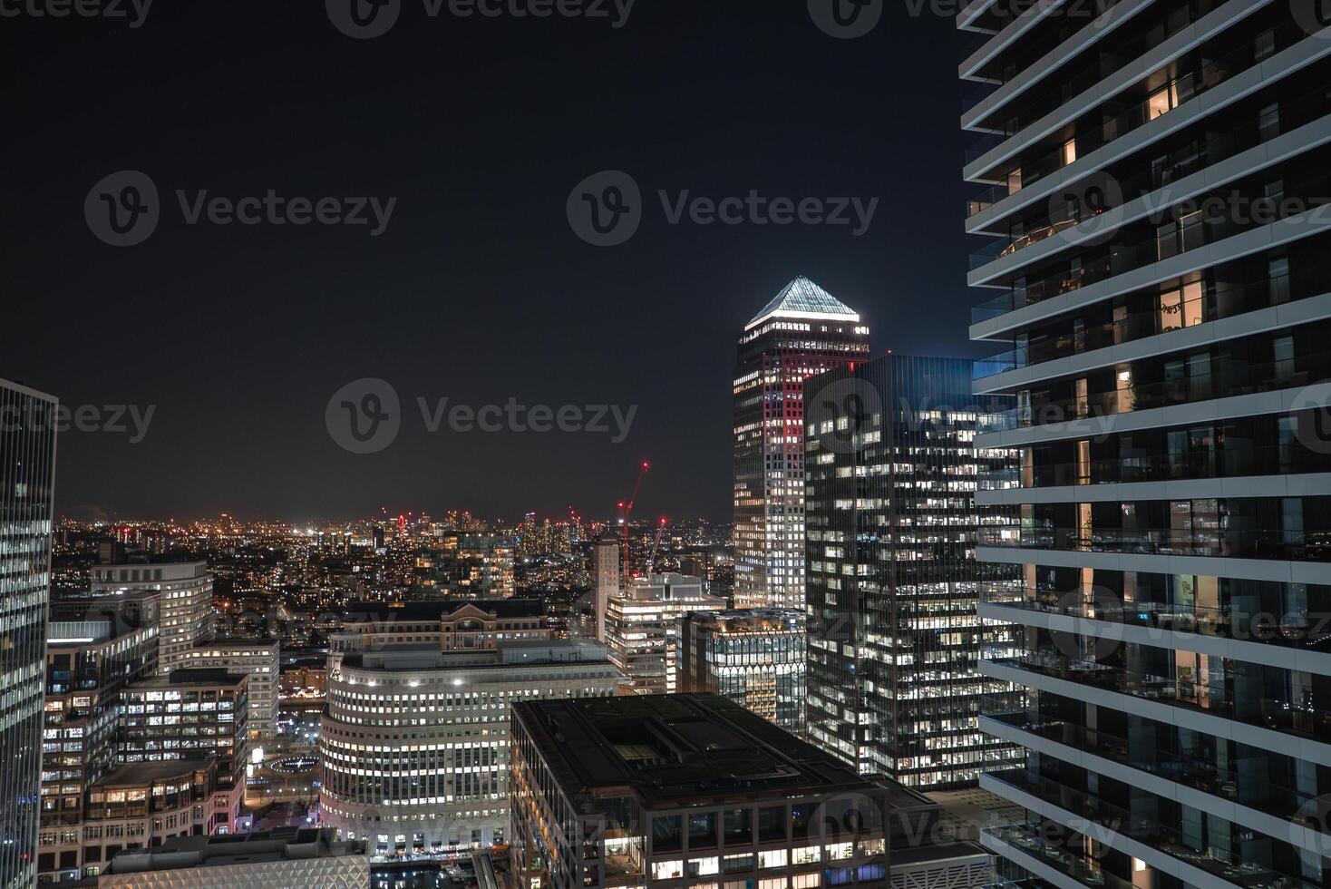Illuminated London cityscape featuring Canary Wharf's skyline, with One Canada Square's pyramid roof, modern high rises, and distant crane lights. photo