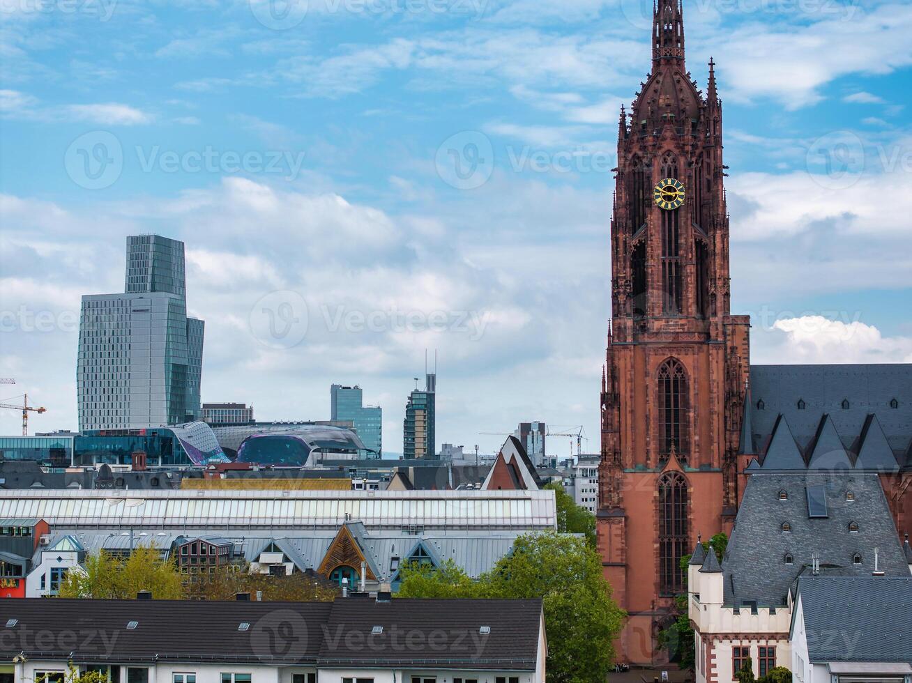 Frankfurt Cathedral's red sandstone facade and clock tower stand out against modern skyscrapers, including the European Central Bank, under a cloudy sky. photo
