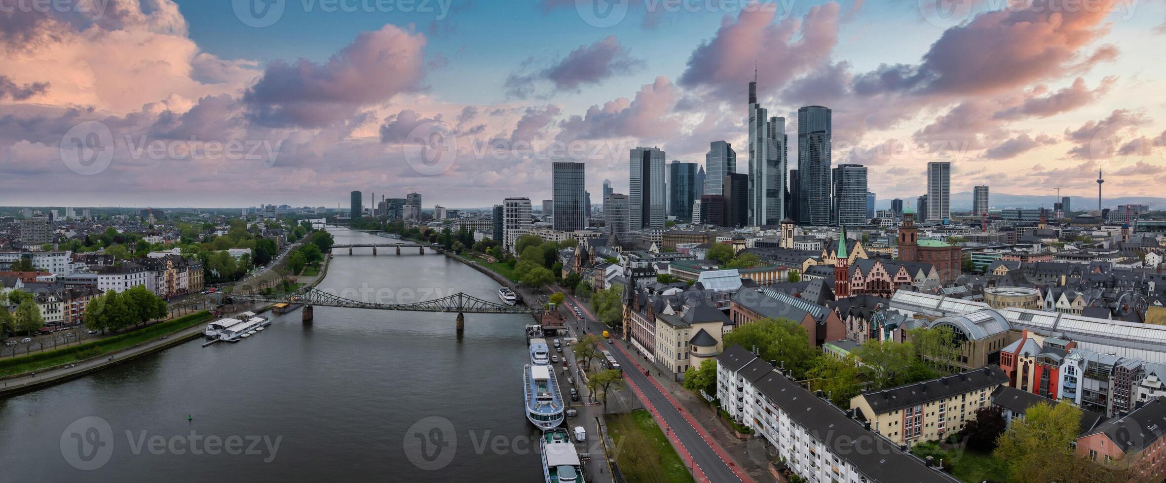 Aerial view of Frankfurt, Germany, featuring the Main River, Commerzbank Tower, Frankfurt Cathedral, Eiserner Steg bridge, and a vibrant sunset sky. photo