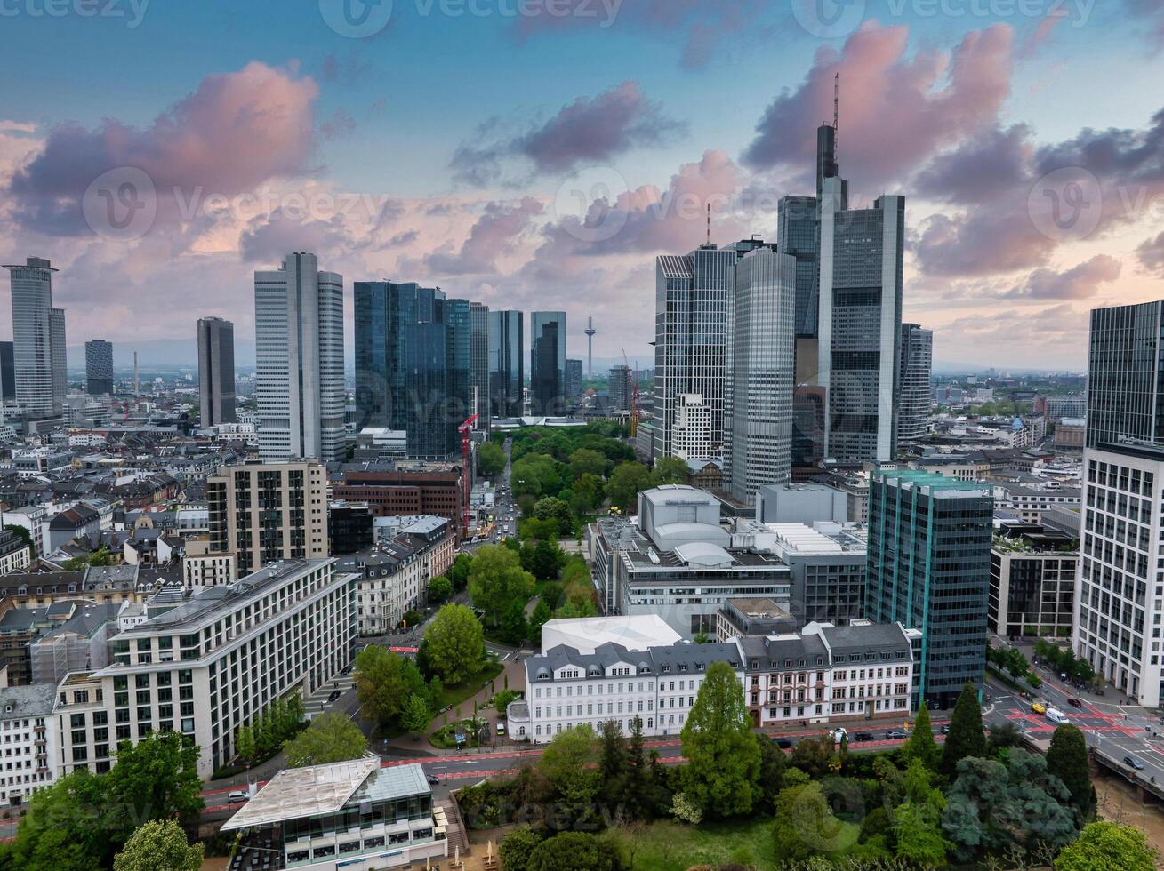 Aerial view of Frankfurt, Germany, featuring modern skyscrapers like the Commerzbank Tower, green spaces, and a sky with soft, colorful clouds. photo