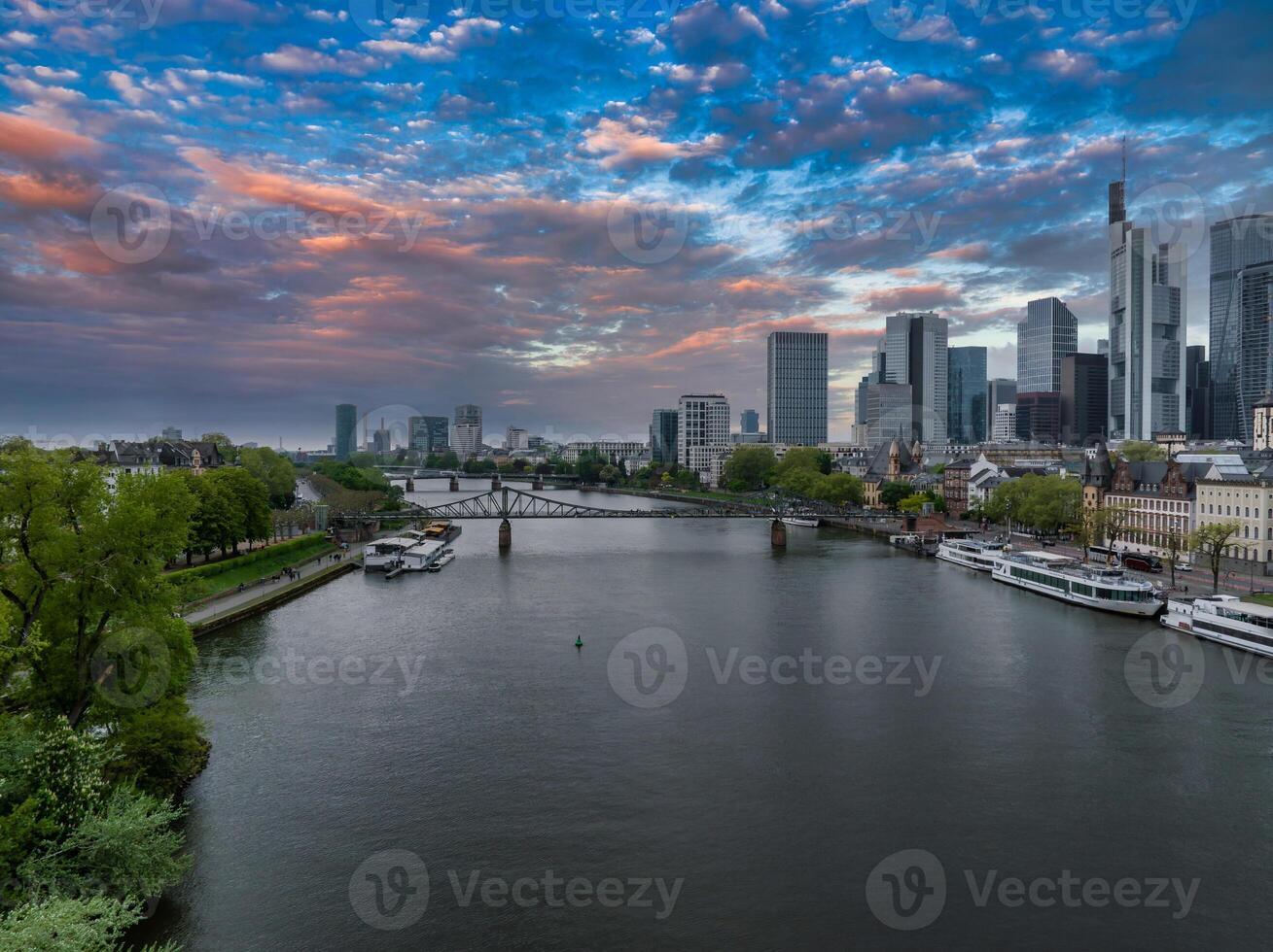 Aerial view of Frankfurt, Germany, featuring the Main River, Commerzbank Tower, Eiserner Steg bridge, and a vibrant sunset with colorful skies. photo