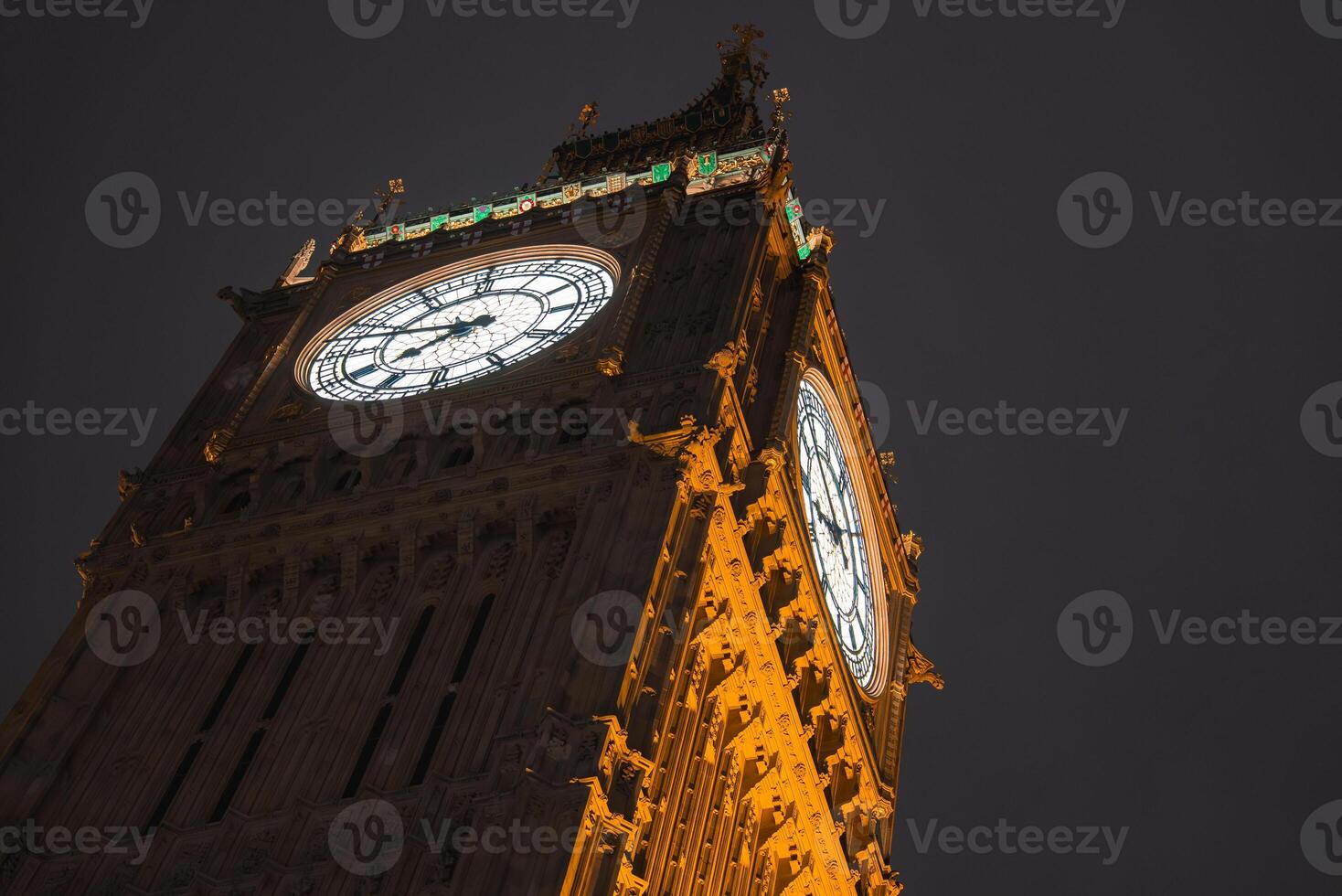 Big Ben, also known as Elizabeth Tower, is seen at night in London, England. The clock faces glow warmly, contrasting with the dark sky above. photo