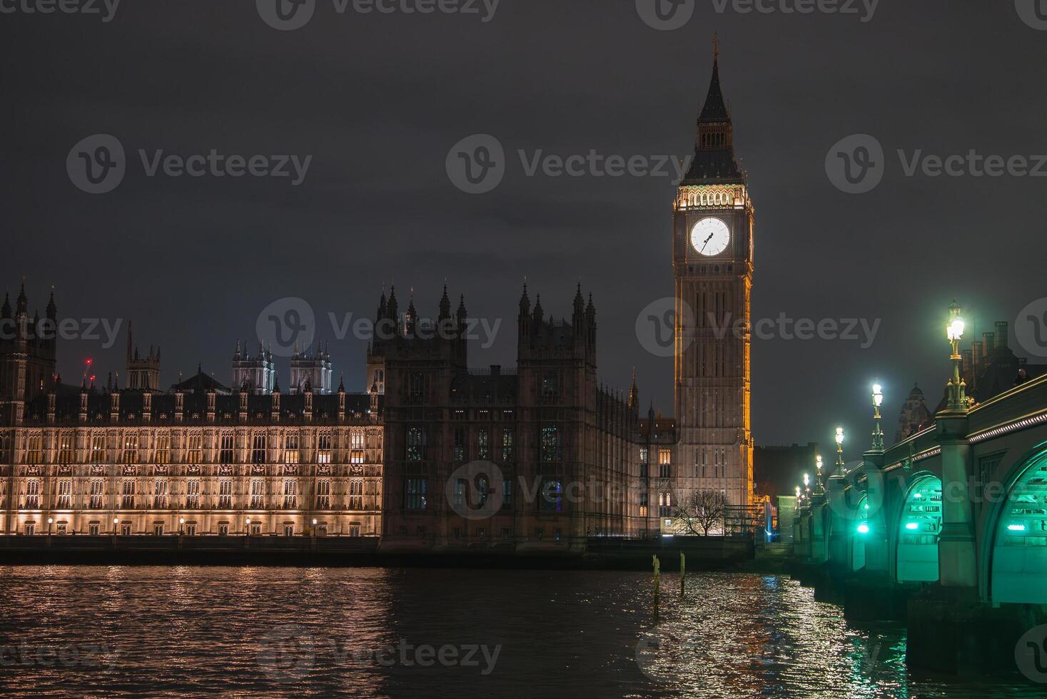 Big Ben and the Palace of Westminster glow against the night sky, with Westminster Bridge's green lights reflecting on the River Thames in London. photo