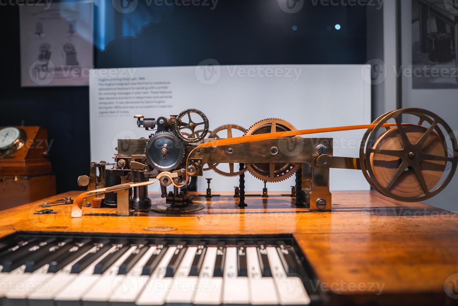 A historical machine with intricate gears, wheels, and levers on a wooden surface. A keyboard in the foreground suggests a musical connection. Museum setting. photo