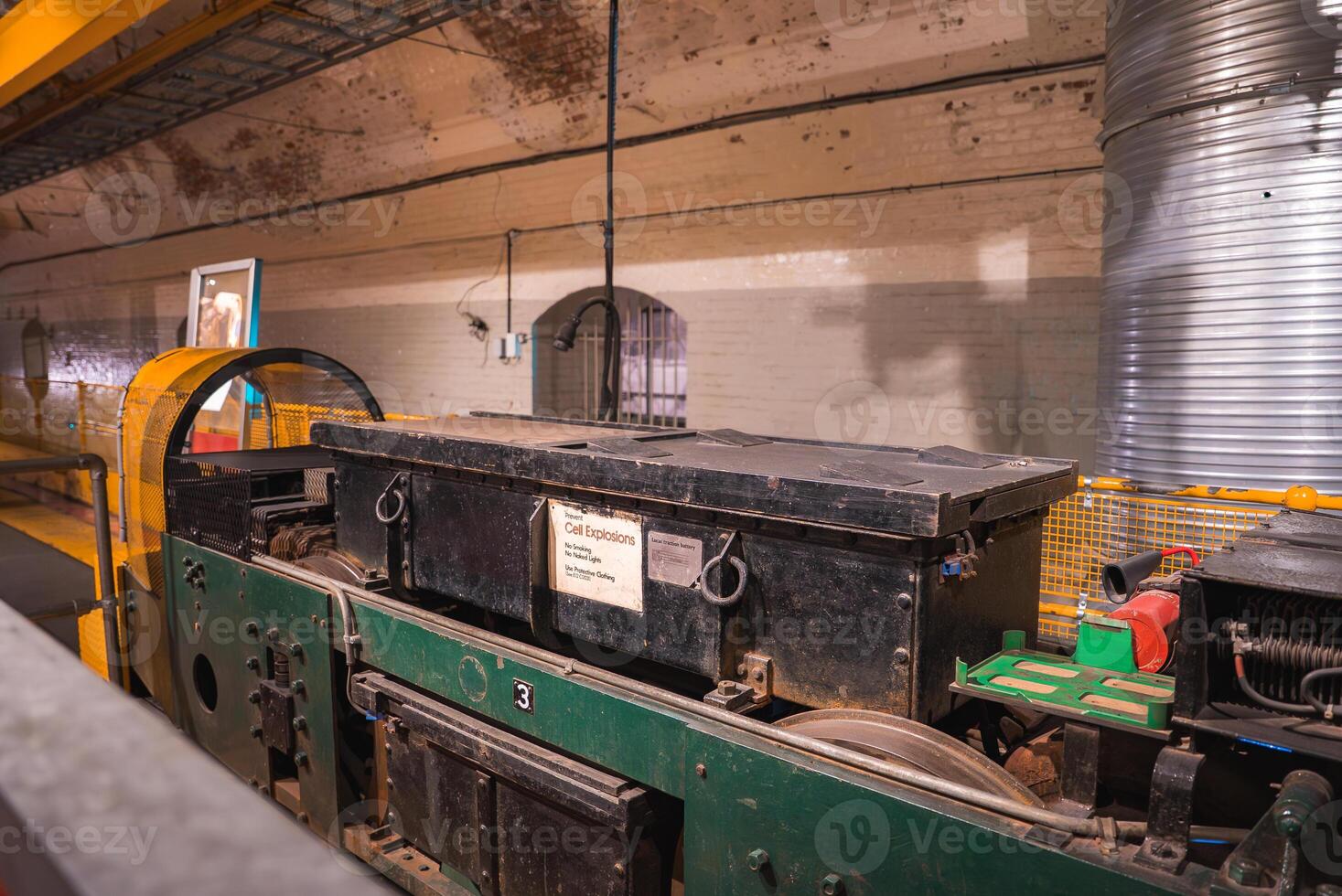 Indoor display of a green and black locomotive labeled 'Cell Explosion' in a brick walled underground space with arched doorways and visible piping. photo