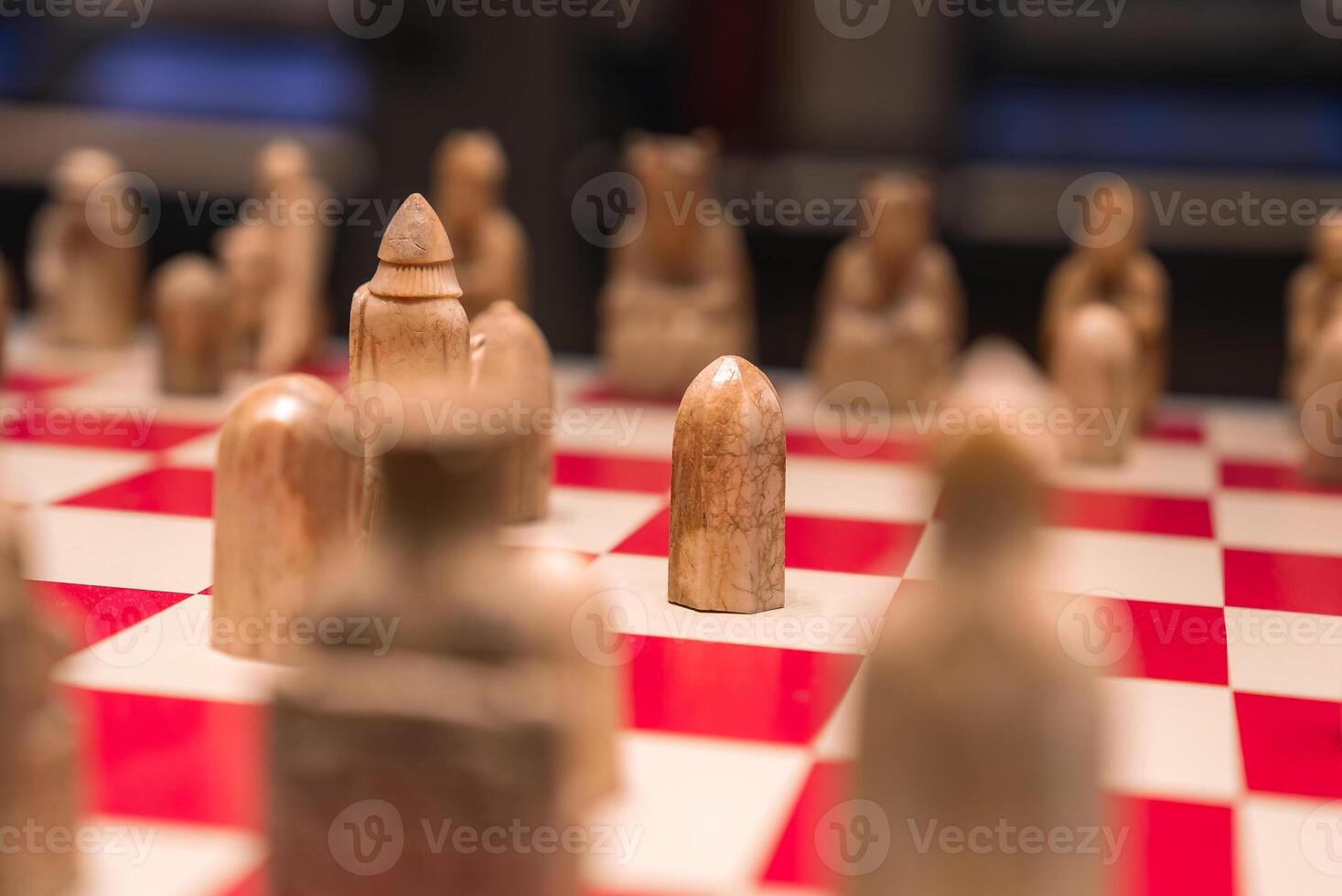 A detailed view of a chessboard with red and white squares, featuring intricately carved chess pieces resembling abstract handcrafted figures. photo