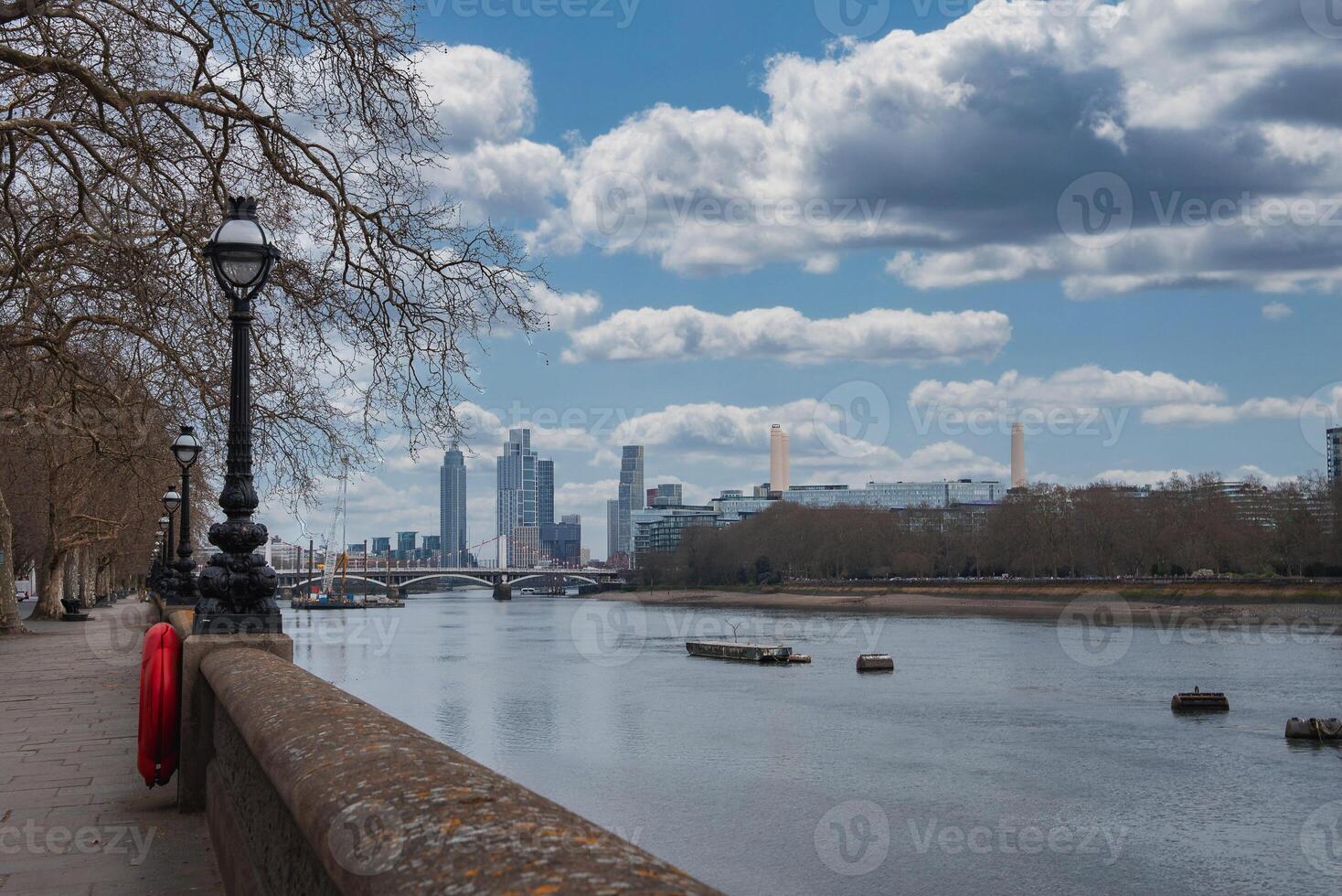 Scenic view of the River Thames in London featuring Battersea Power Station, modern skyscrapers, a riverside walkway, and bare winter trees. photo