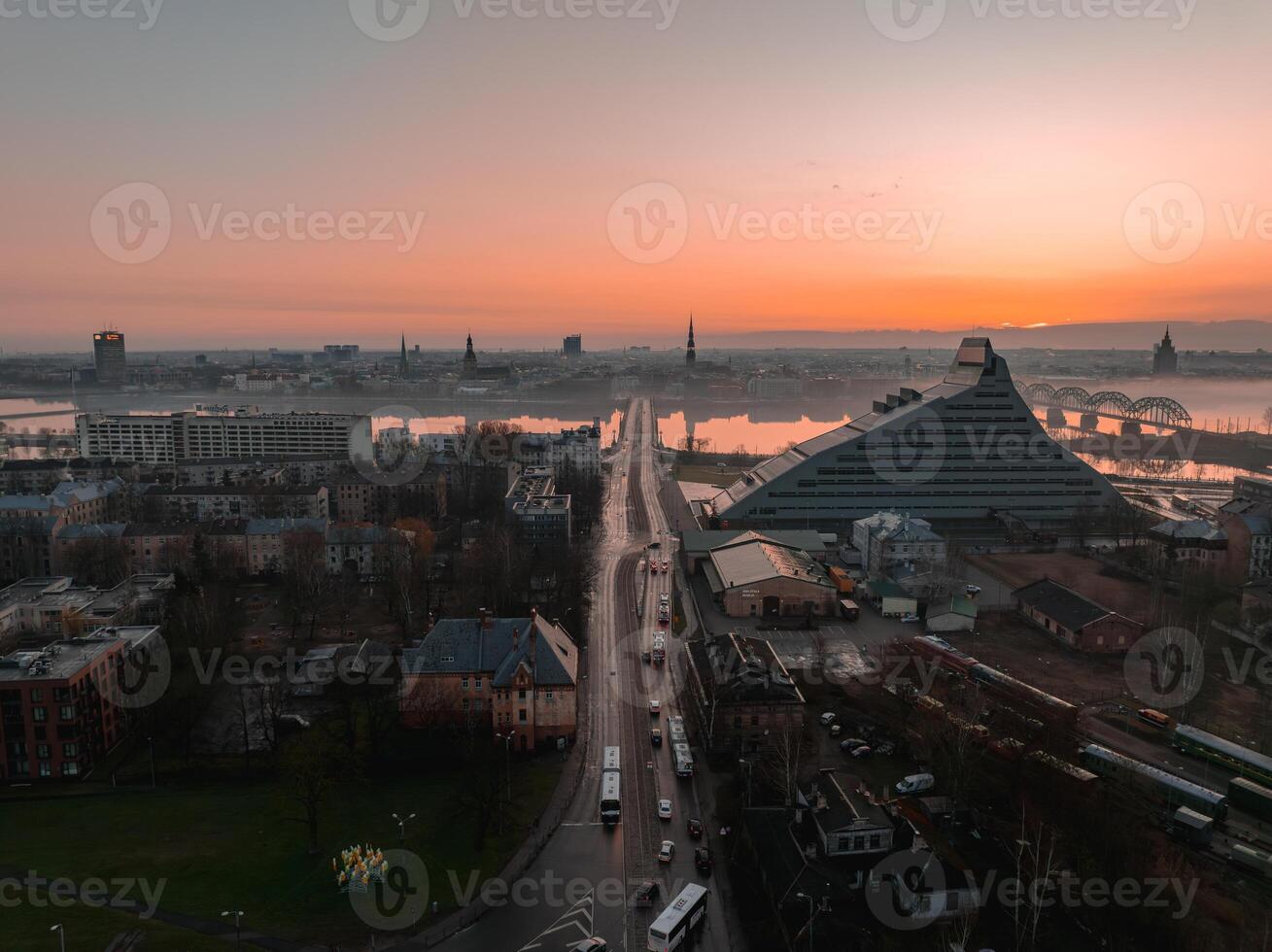 Morning view of Riga, Latvia, featuring the National Library, Daugava River, historic church spires, railway bridge, and urban streets with activity. photo