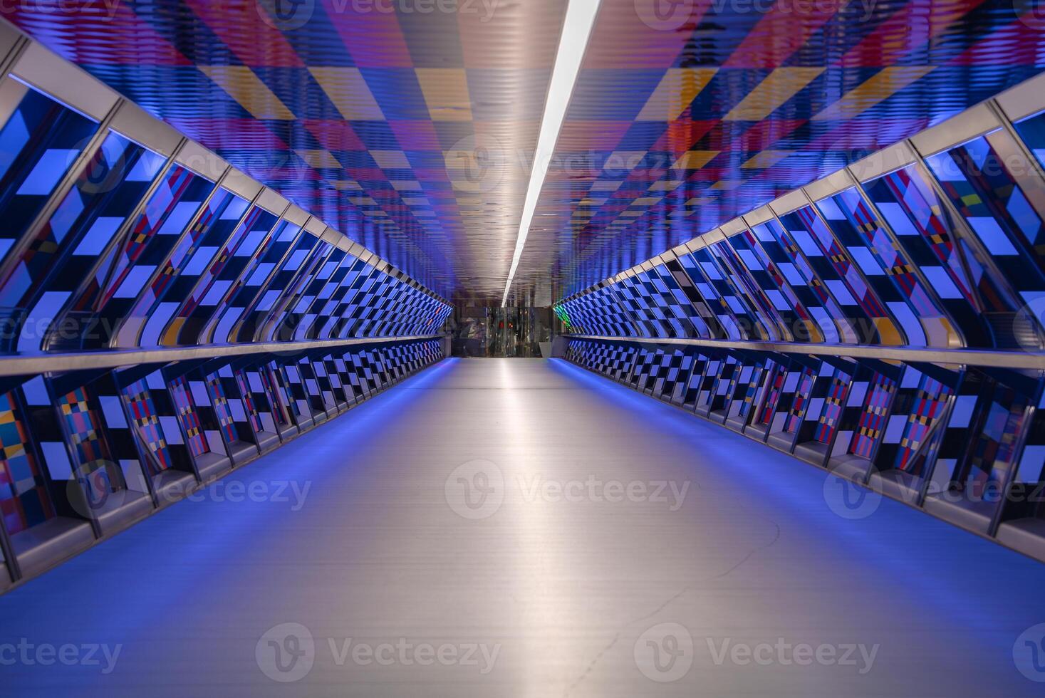 A modern pedestrian tunnel in London featuring a vibrant checkerboard pattern, soft blue lighting, and a symmetrical geometric design leading to a glass exit. photo
