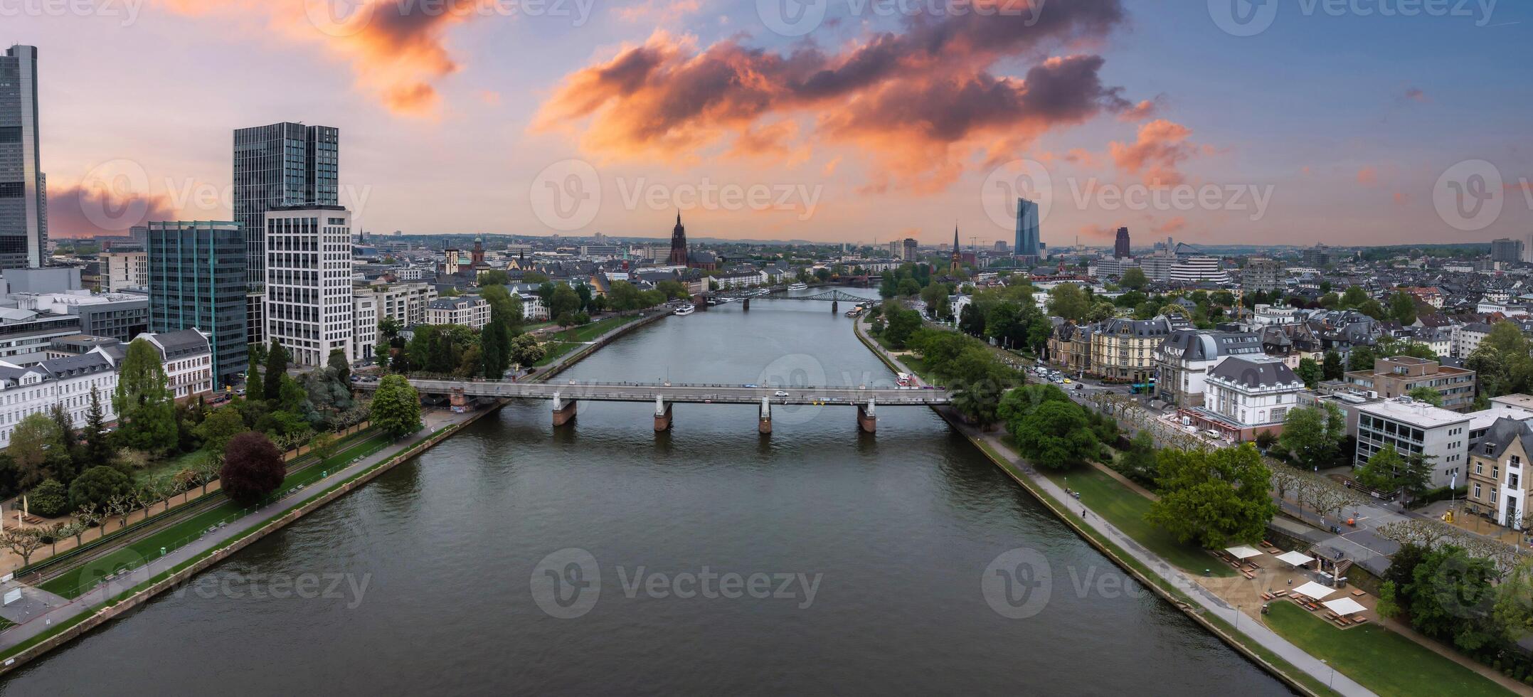 Aerial view of Frankfurt, Germany, during sunset. The Main River flows through the city, with skyscrapers on the left and historic buildings on the right. photo