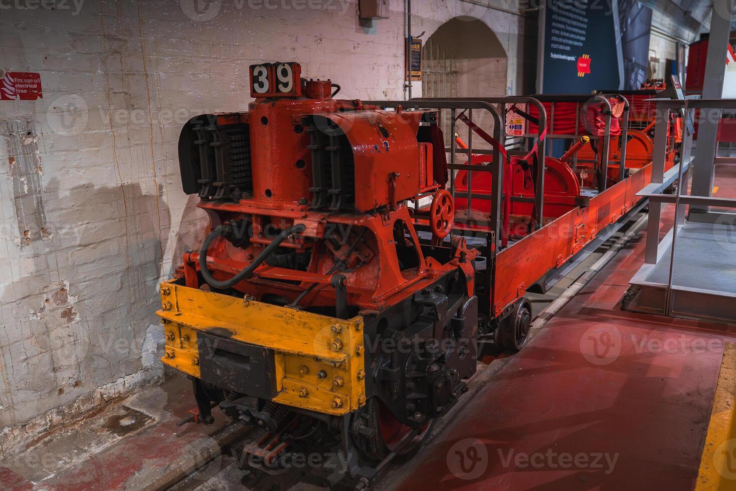 A red and yellow industrial locomotive with number 39 on tracks indoors, set against brick walls and arched doorways in a historical museum setting. photo