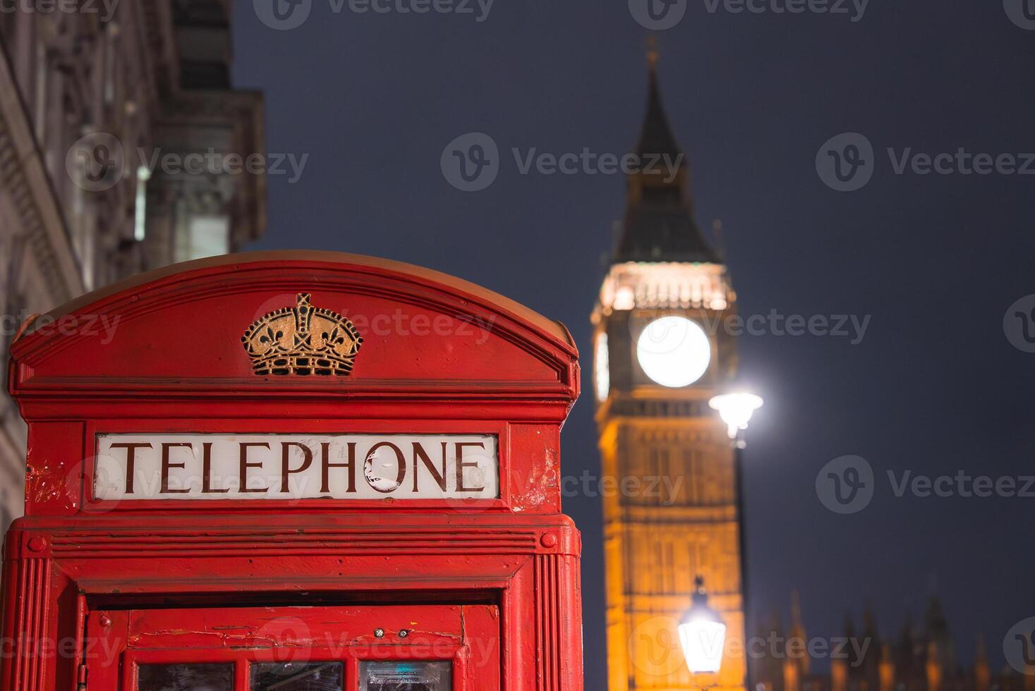 A red British telephone box stands in the foreground with Big Ben and the Palace of Westminster glowing against the night sky in London. photo