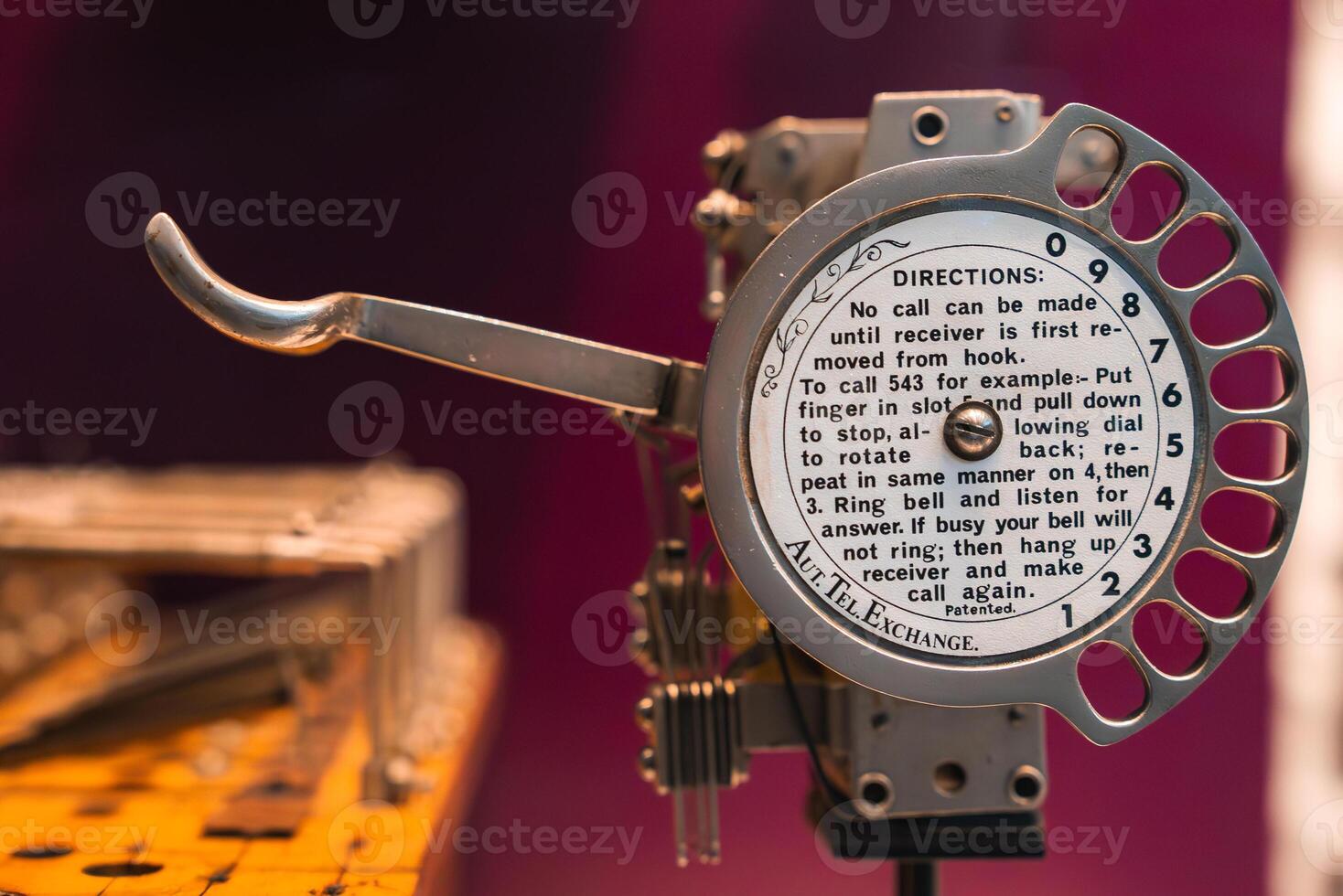 Metallic rotary telephone dial with numbered slots and printed instructions referencing an Autel Exchange, set against a blurred warm toned background. photo