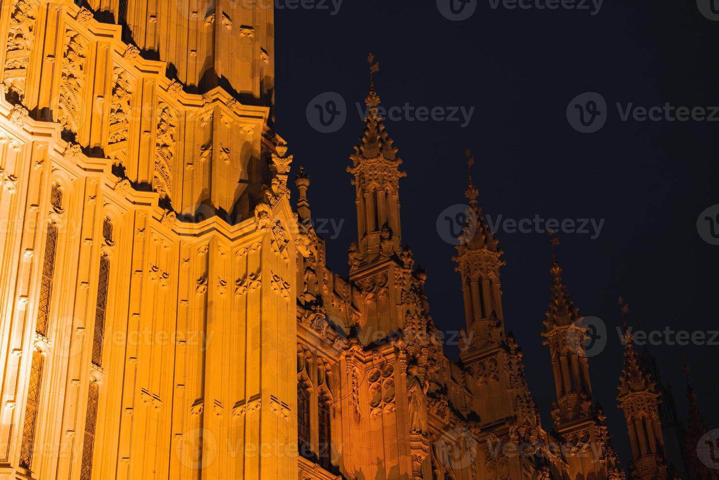 Detailed view of the Palace of Westminster in London, featuring illuminated spires and ornate carvings against a dark night sky. photo