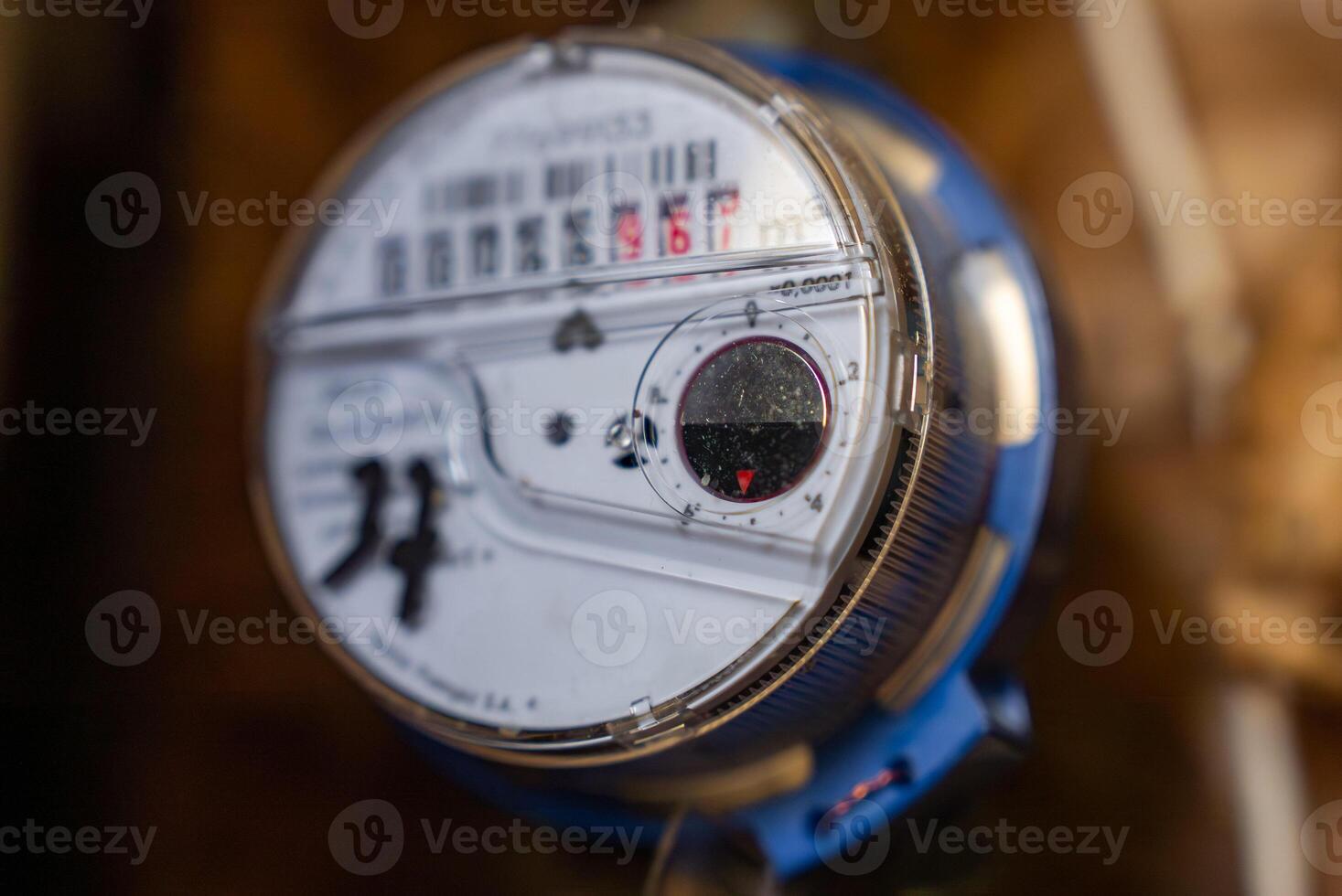 Close up view of a water meter with a clear casing, showing a white dial, black and red counters, a red gauge, and visible brand and model details. photo
