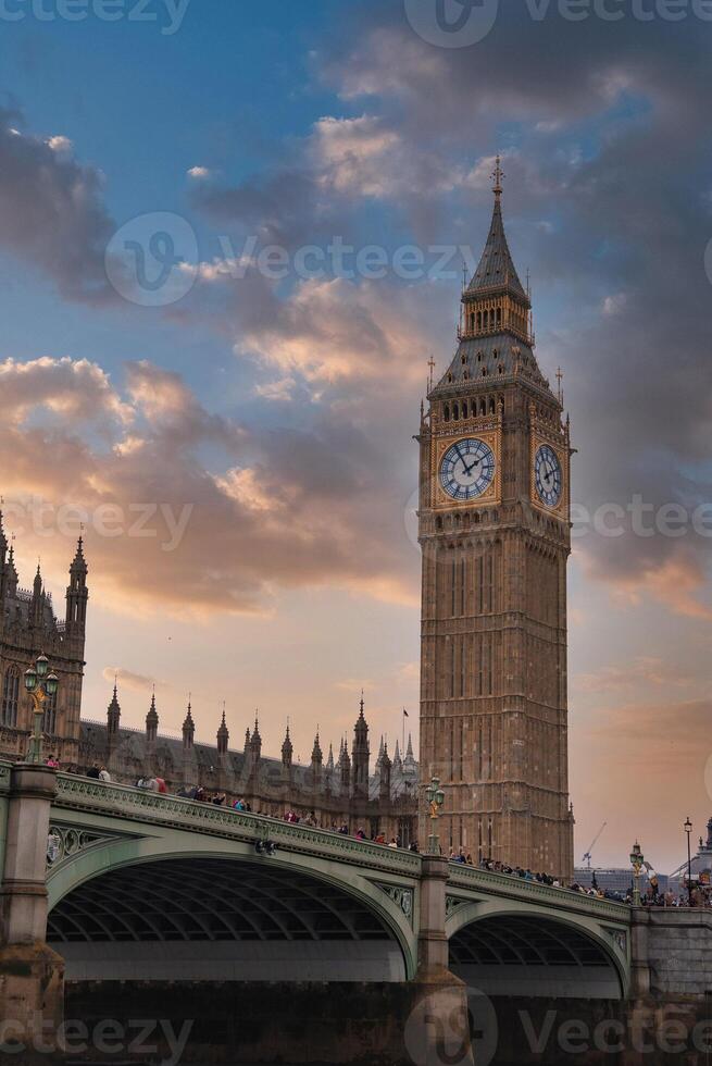 Elizabeth Tower, also known as Big Ben, stands beside the Palace of Westminster. Westminster Bridge crosses the River Thames under a dramatic sky. photo