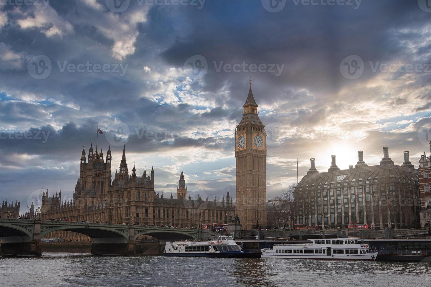 Big Ben and the Palace of Westminster stand by the River Thames in London. Westminster Bridge crosses the river, with boats docked nearby. photo