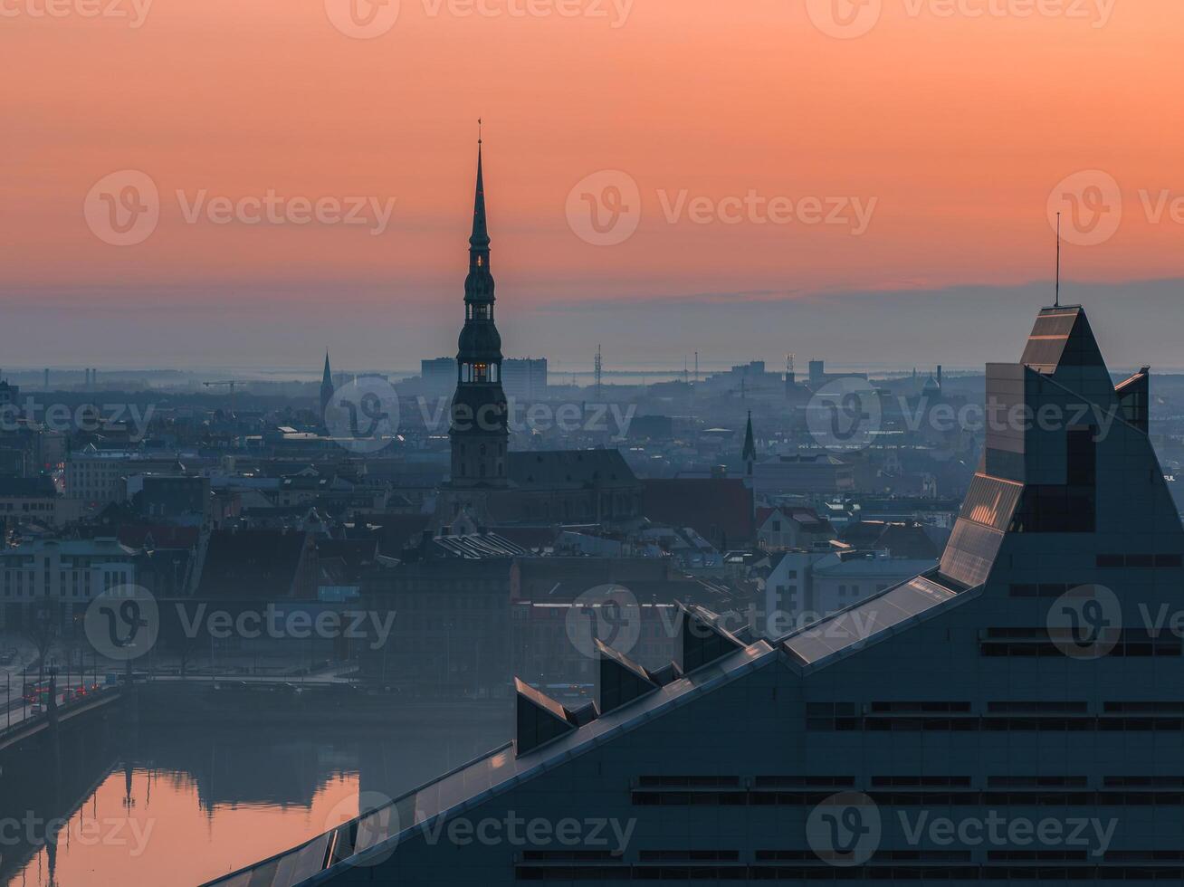 Serene sunrise over Riga, Latvia, featuring St. Peter's Church spire, historic cityscape, modern National Library, and reflections on the Daugava River. photo
