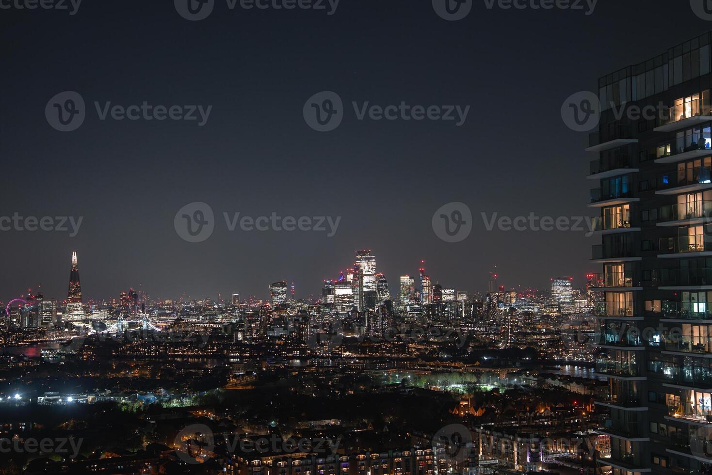 London's illuminated skyline at night with The Shard on the left, City of London skyscrapers in the center, and urban areas in the foreground. photo