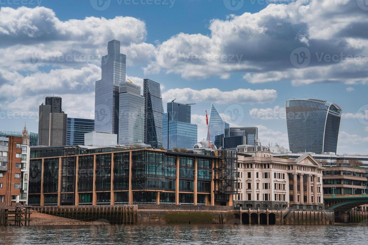 The London skyline features the Walkie Talkie and Leadenhall buildings, with historic riverside architecture and the Thames River under a partly cloudy sky. photo