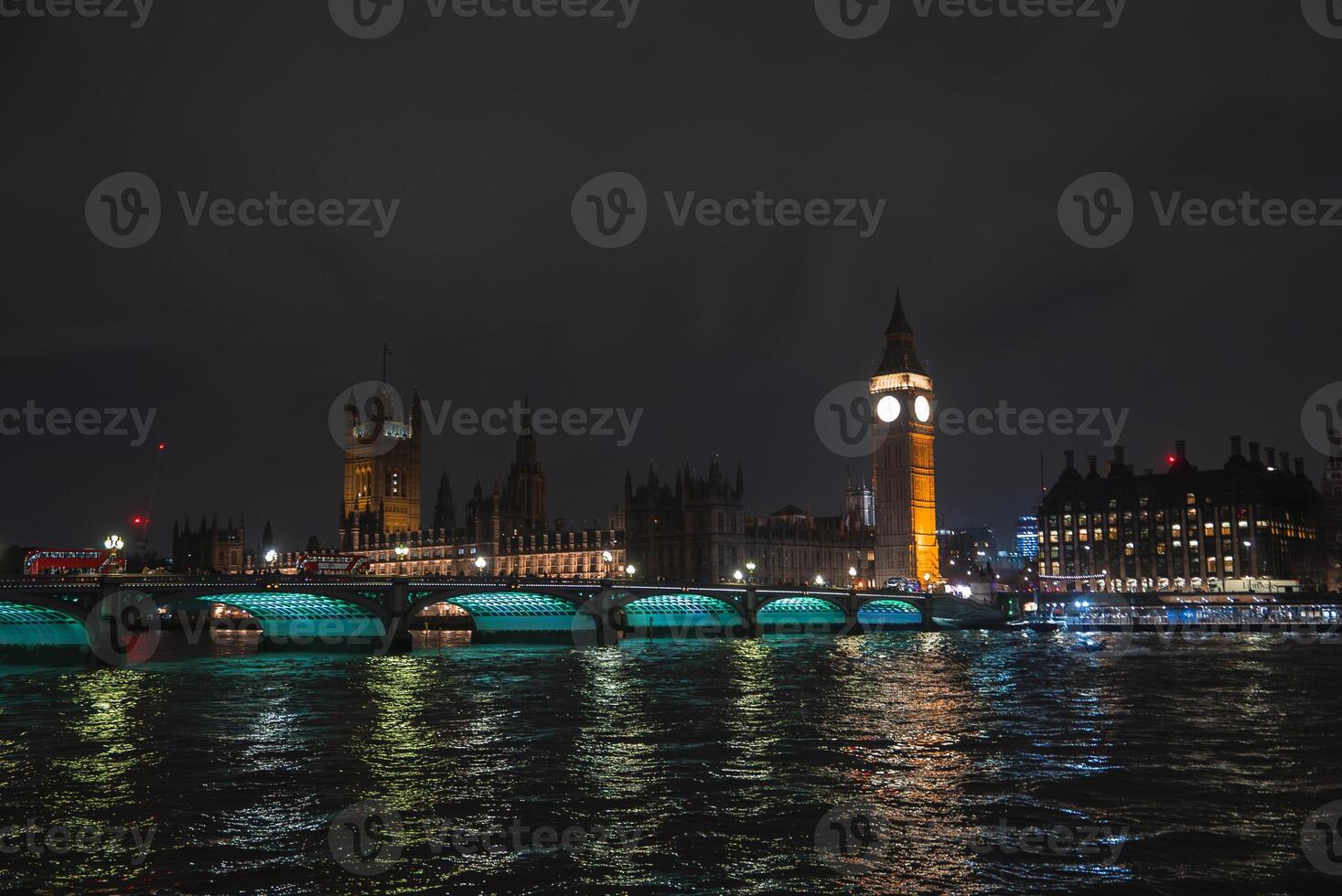 Illuminated Big Ben and Houses of Parliament at night with Westminster Bridge spanning the River Thames, green lights reflecting on the water. photo