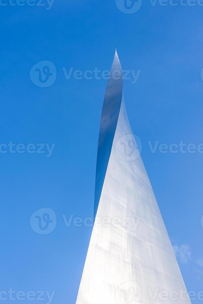 A sleek metallic structure with a sharp, tapering point and reflective surface set against a clear blue sky, showcasing modern architectural design. photo