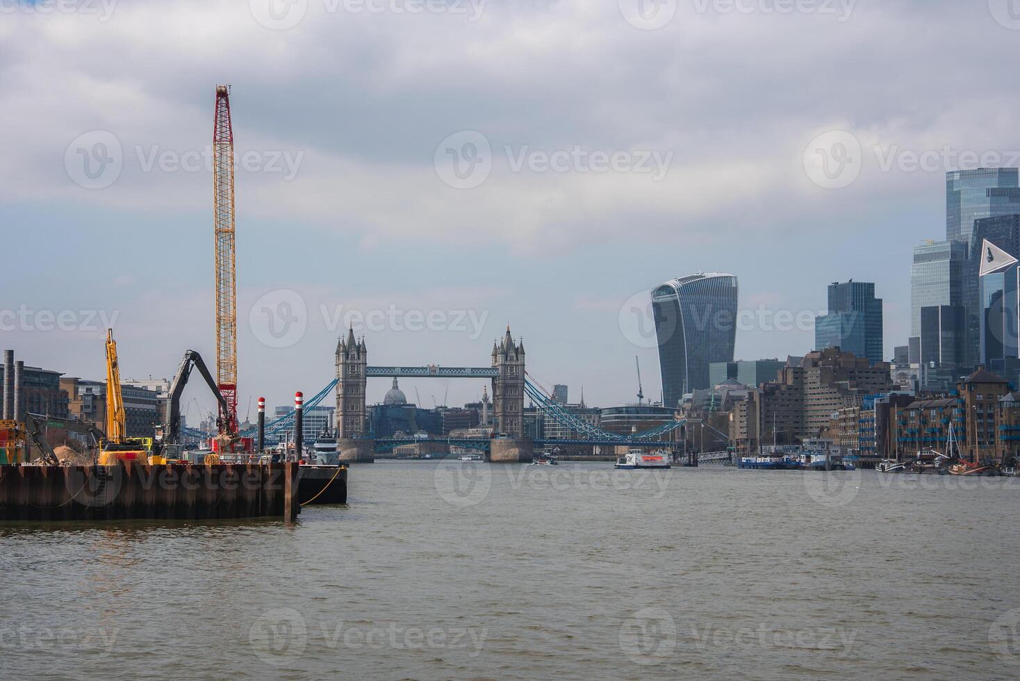 View of Tower Bridge over the River Thames in London, with modern skyscrapers like the Walkie Talkie building and construction cranes on the riverbank. photo