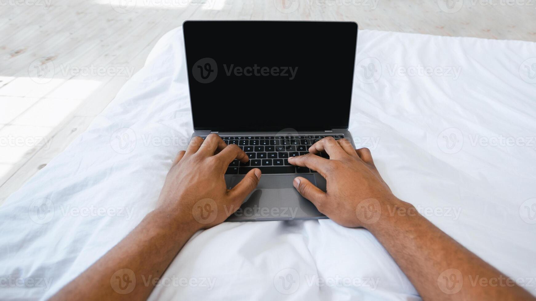 Black Male Hands Using Laptop With Blank Screen Working Online Lying In Bed At Home. Internet Website Advertising, African Freelancer Typing On Computer Keyboard. Cropped, Mockup, POV photo