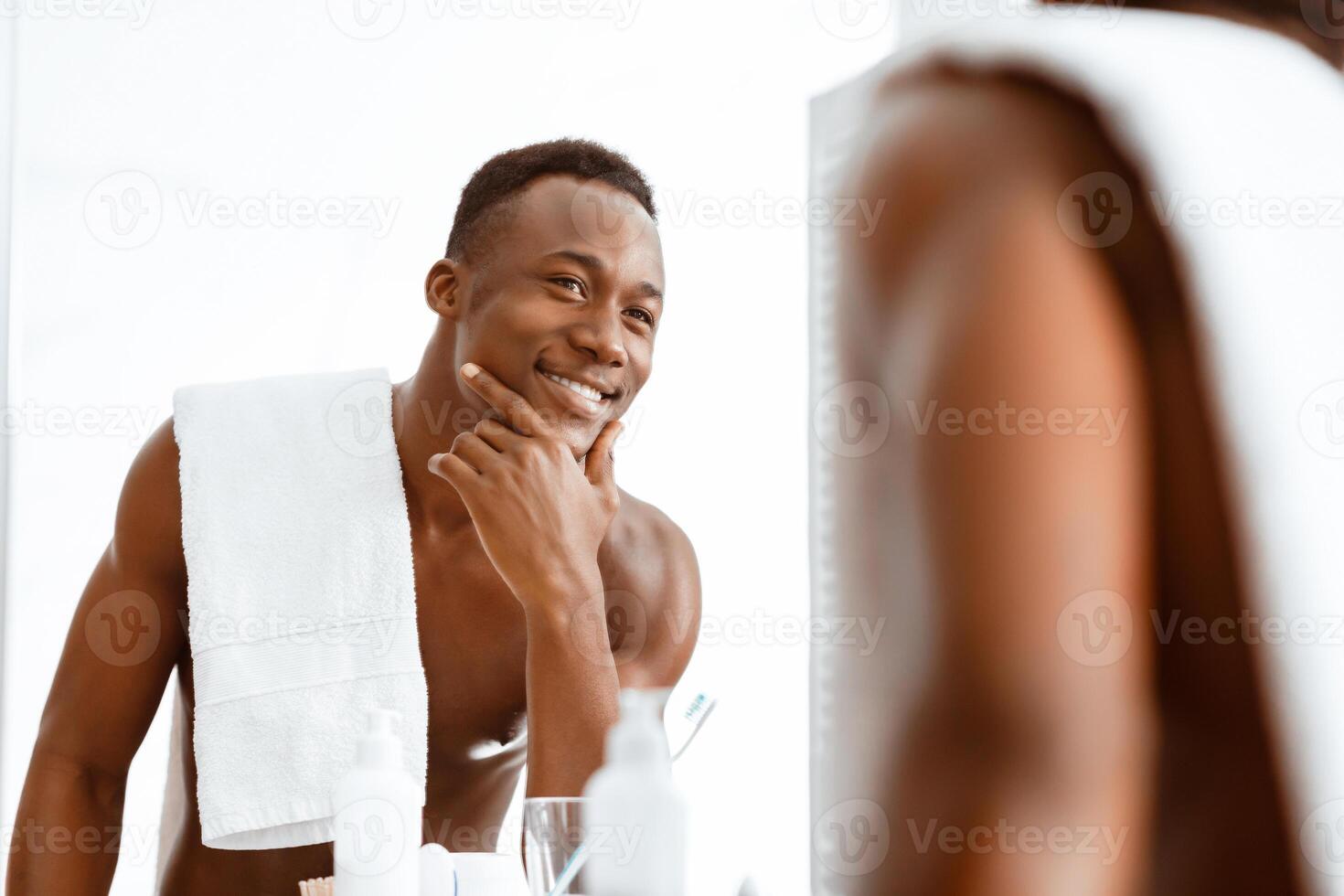 Handsome Muscular Black Man Touching Smooth Well-Shaved Face Looking At His Reflection In Mirror Standing Shirtless In Bathroom At Home. Male Beauty, Daily Selfcare And Bodycare Routine photo