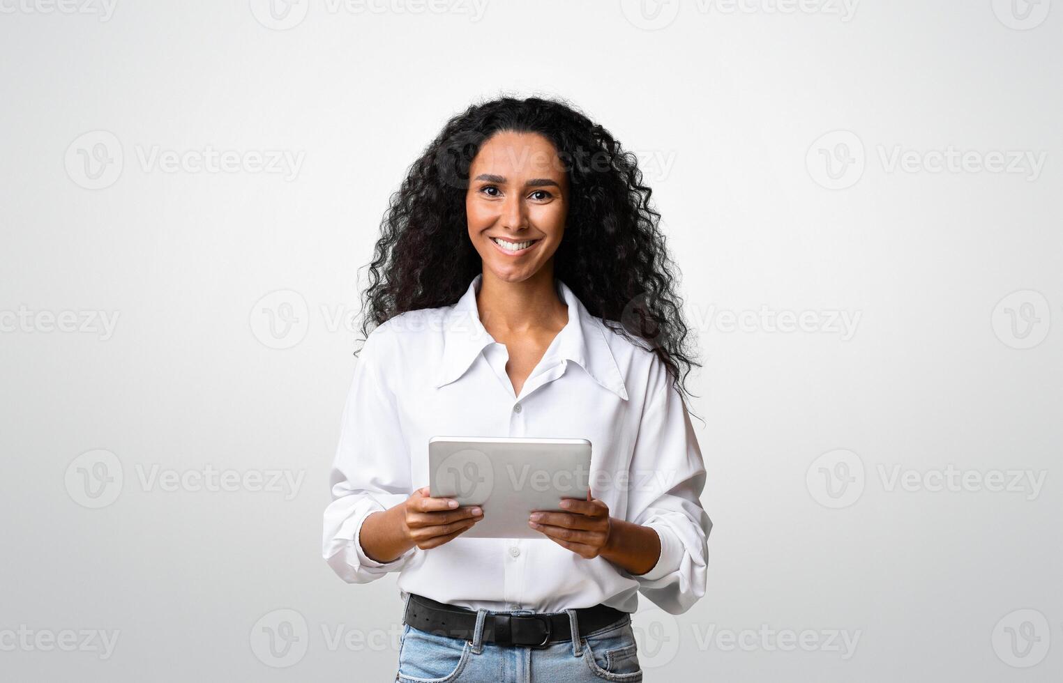 Curly Brunette Woman Posing With Digital Tablet In Hands Over Yellow Background In Studio, Smiling At Camera, Copy Space photo