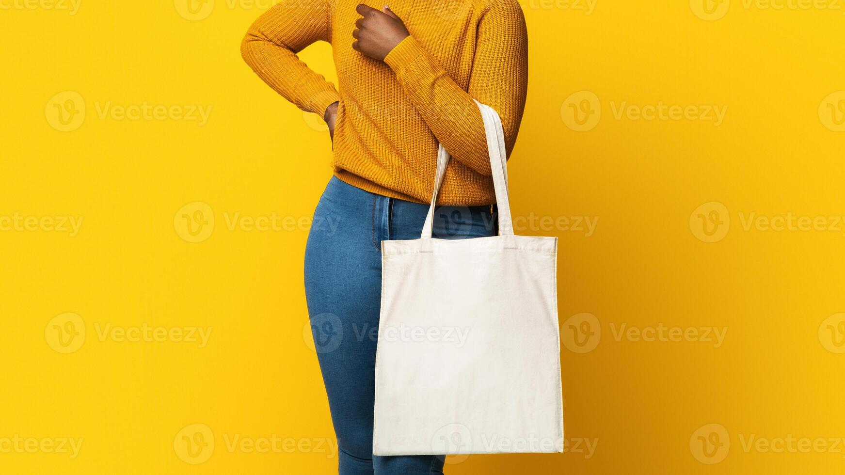 Mockup For Design. Cheerful African American Lady Holding Blank White Eco Tote Canvas Bag With Copy Space, Positive Black Female Posing Over Yellow Background In Studio, Smiling At Camera photo