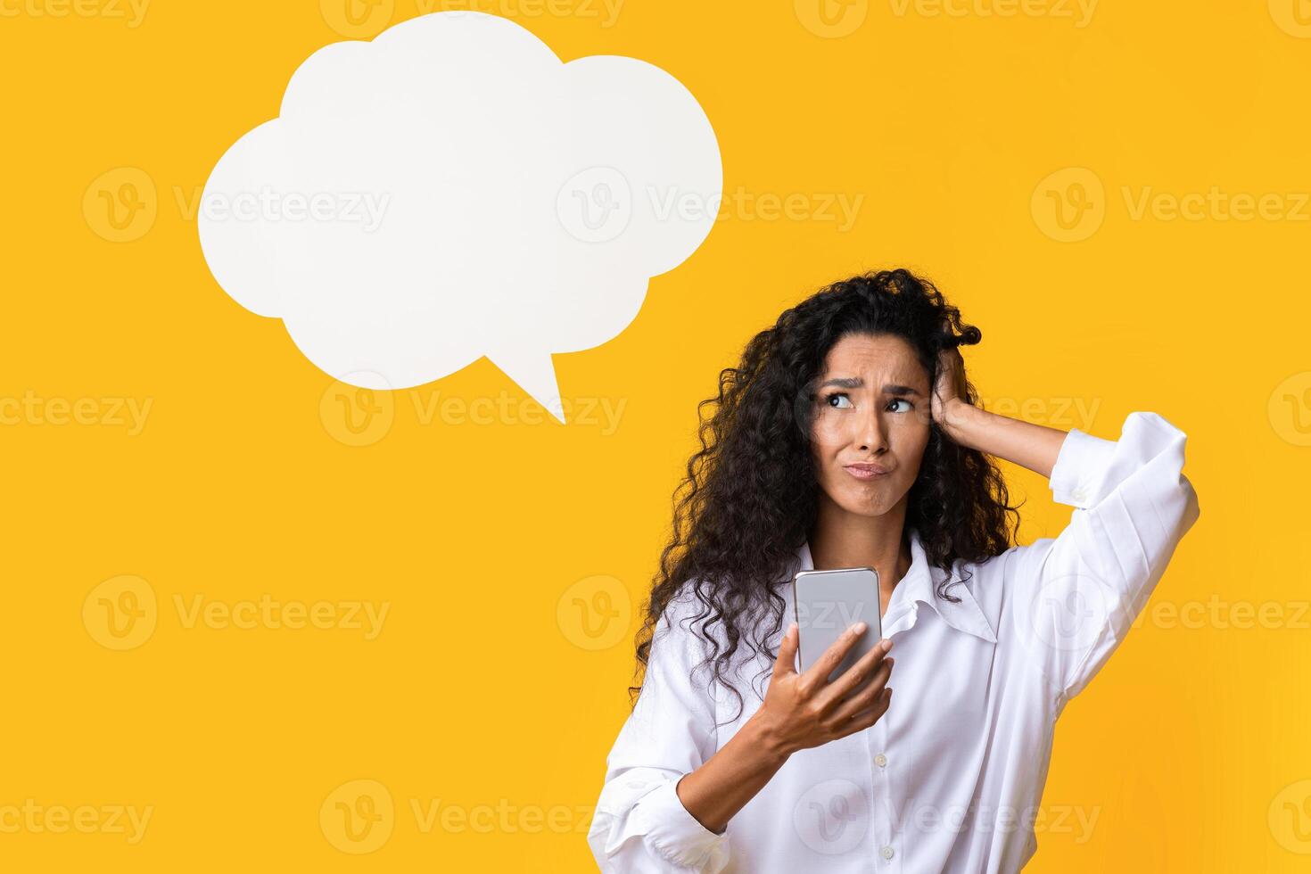 Doubtful Brunette Woman Holding Smartphone And Looking Away At Copy Space With Pensive Face Expression, Thinking About Mobile Online Offer, Standing Over Yellow Studio Background, Panorama, Copy Space photo