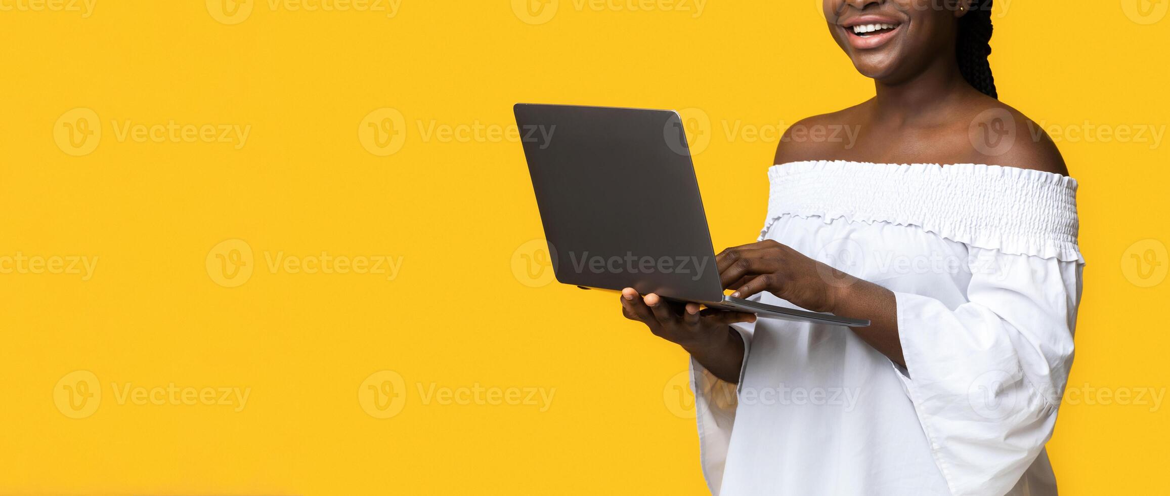 Cheerful Black Woman Posing With Laptop In Hands Over Yellow Studio Background, Working Remotely, Doing Online Business, Checking New Website, Browsing Social Media And Smiling At Camera, Copy Space photo
