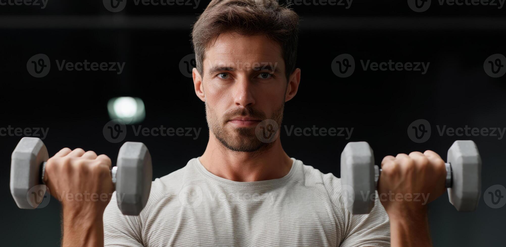 A determined man is lifting dumbbells in a gym, focusing on strength training. His intense expression shows dedication to improving his physical fitness during a morning workout. photo