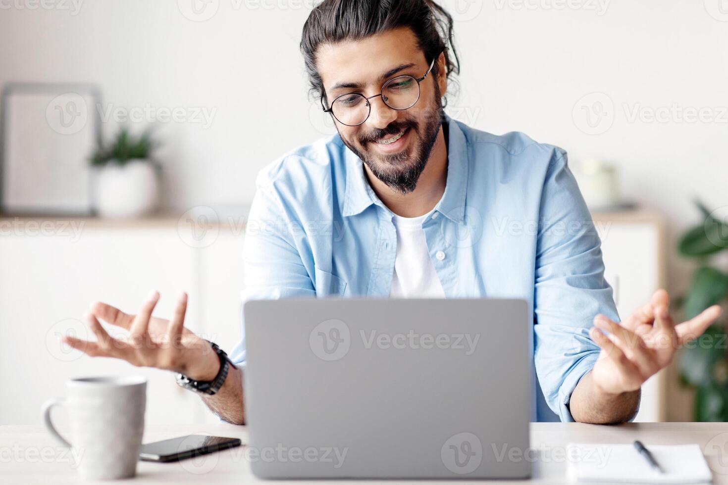 Online Tutoring. Friendly Indian Man Having Conference With Laptop, Teaching Foreign Languages, Talking And Gesturing At Camera During Web Call, Sitting At Desk In Home Office, Copy Space photo