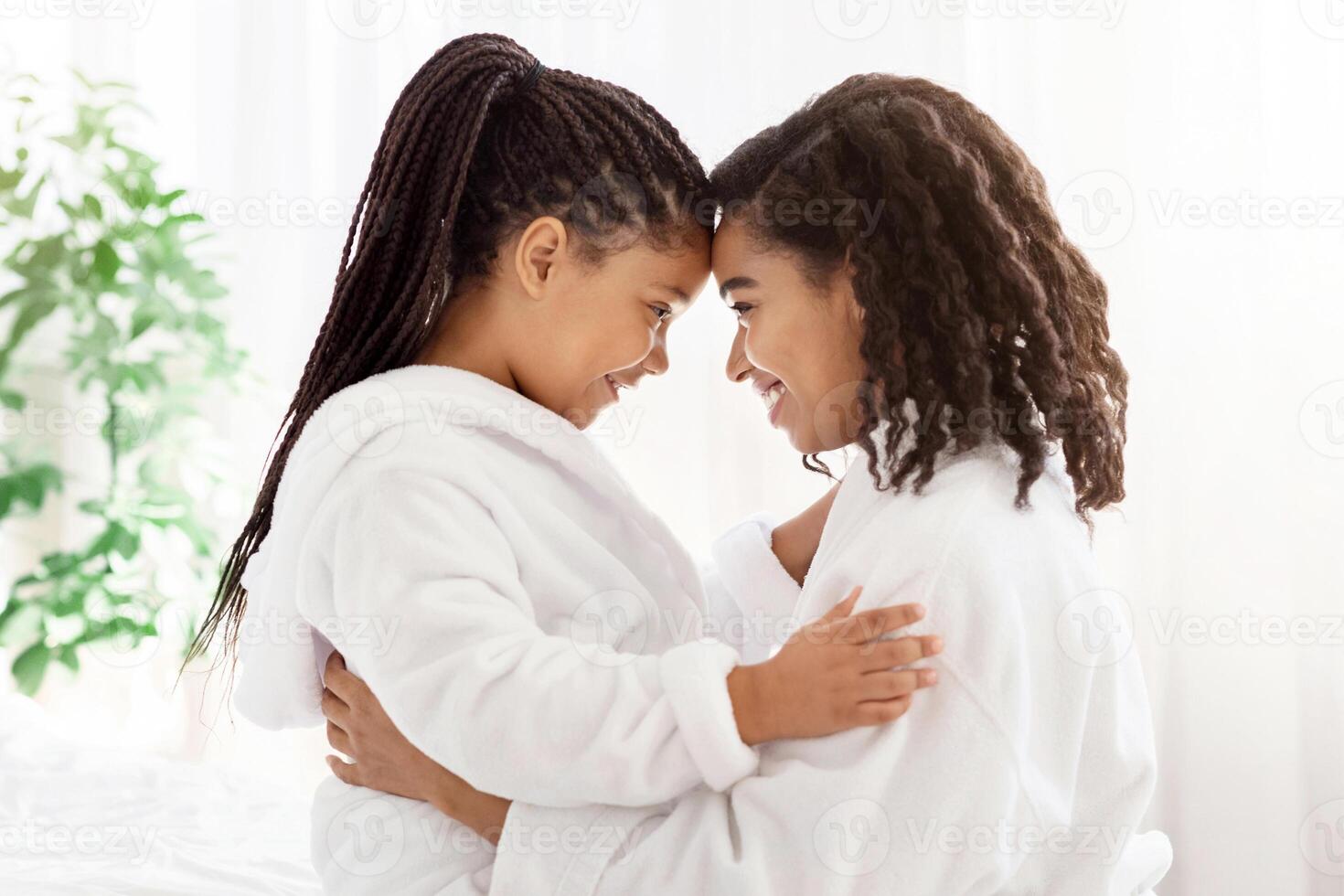 Portrait Of Happy Embracing Black Mom And Daughter In Bathrobes At Home, Bonding With Each Other, Touching Foreheads, Having Fun And Enjoying Spending Time Together, Side View With Copy Space photo