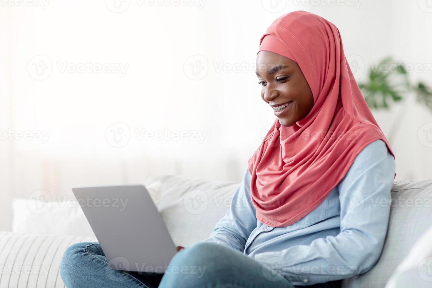 Internet Shopping. Young Black Muslim Lady In Hijab Buying Things Online With Laptop At Home, Purchasing Goods From Website, Sitting On Couch In Living Room With Computer On Laps, Copy Space photo