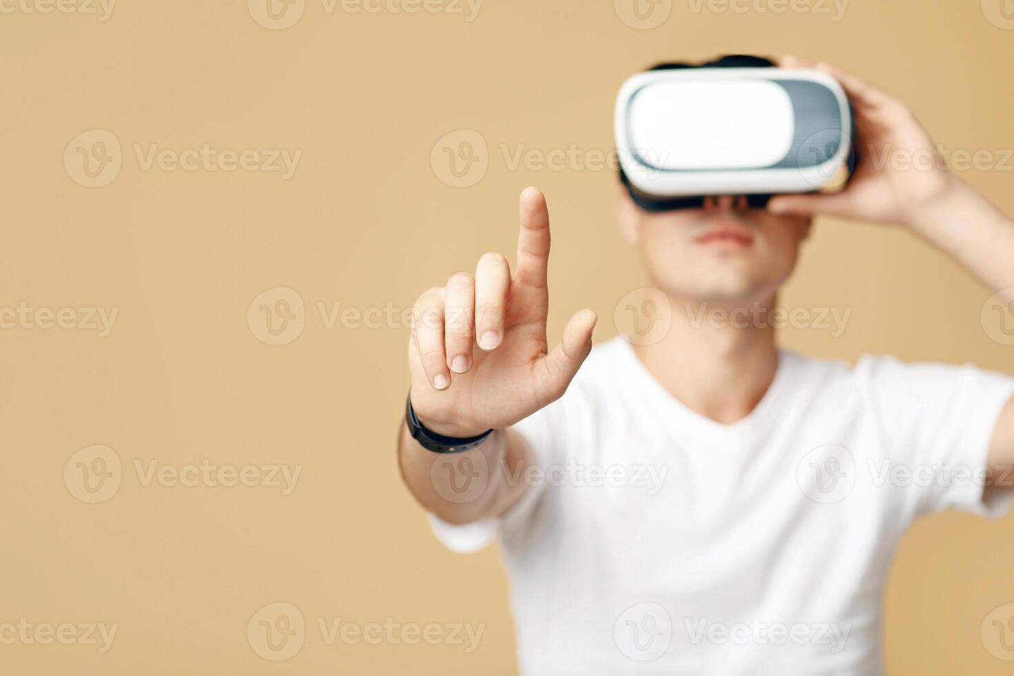 Man playing simulation games with headset and gesturing with his finger. Concentrated young man student in white t-shirt and virtual reality glasses touches blank space, isolated on light background photo
