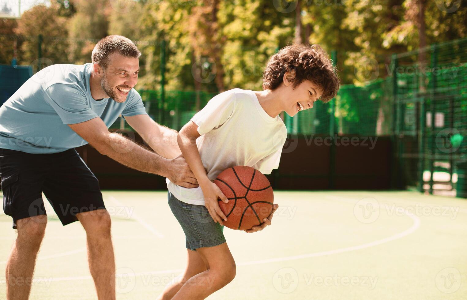 Bonding Concept. Portrait in action of father and son playing basketball together, man trying to catch the ball photo