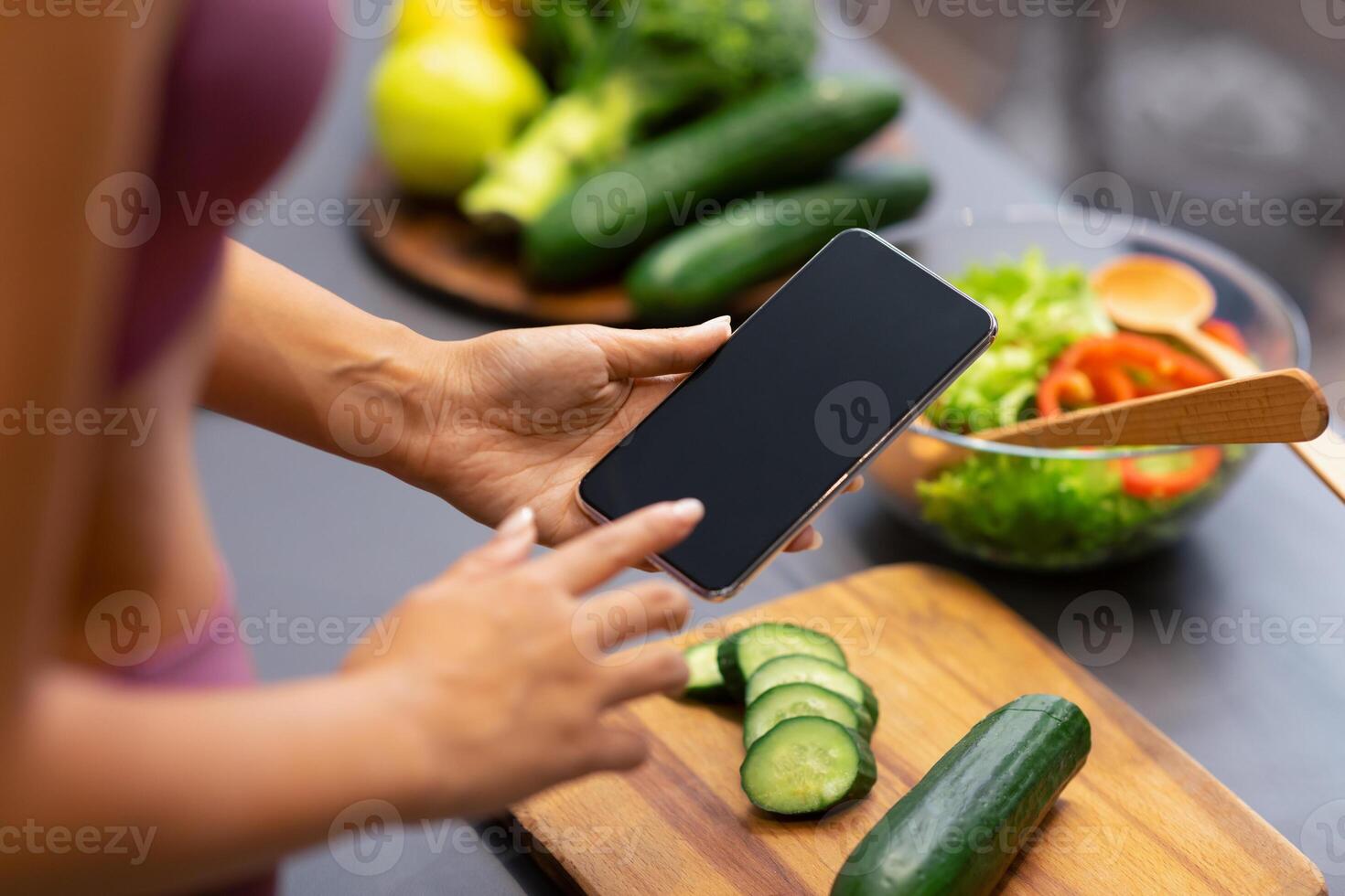 Weight Loss Application. Unrecognizable Woman Using Mobile Phone With Empty Screen, Cooking And Searching Recipes For Slimming Preparing Healthy Dinner In Modern Kitchen At Home. Cropped, Mockup photo